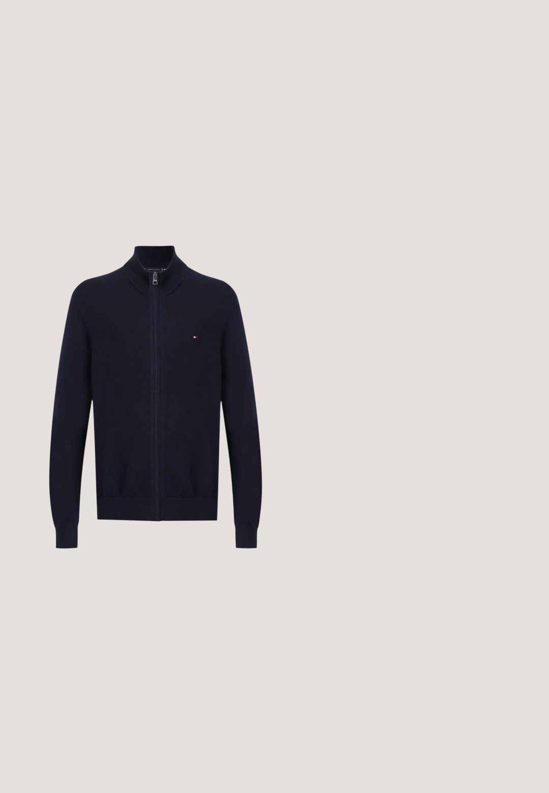 Pull bleu marine à fermeture éclair intégrale, col, poignets et ourlet côtelés, avec un petit logo rouge, blanc et bleu sur la poitrine.; T-shirt en coton bleu marine avec des manches courtes, un col rond, et un petit logo blanc "HILFIGER 1985" sur la poitrine. Texture douce.; Pantalons marron à jambes droites en tissu texturé, avec une fermeture à bouton et une taille standard, dotés de poches latérales et de coutures ajustées.; Chaussure habillée en cuir marron foncé à lacets flottant au-dessus d'un tapis beige clair avec une table brillante de couleur ambre en arrière-plan.; Sac fourre-tout en toile beige avec des poignées blanches, présentant un patch décoratif sur un côté. Le sac est rectangulaire avec une forme structurée.; Ceinture en cuir brun avec une boucle rectangulaire en métal noir, présentant des détails de couture le long des bords et une texture lisse.