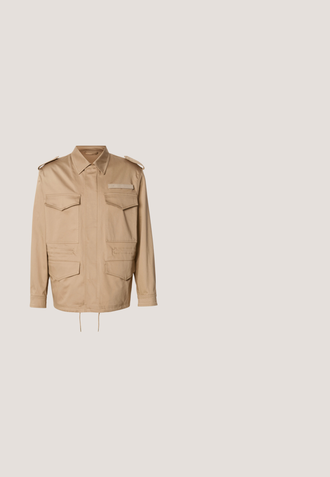 Chaqueta utilitaria beige con dos bolsillos en el pecho y dos bolsillos inferiores. Cuenta con cuello con solapa y hombreras con botones. Bajo ajustable con cordón.; Jersey beige de manga larga con cuello redondo, textura fina de canalé horizontal y pequeño parche triangular con logo en el bajo.; Polo marrón hecho de algodón suave con un cuello clásico y mangas cortas. Presenta un pequeño parche de logo en el pecho.; Jeans de mezclilla de pierna ancha en un tono azul oscuro, con pliegues frontales y costuras naranjas, presentados sobre fondo blanco.; Zapatillas deportivas negras con una mezcla de materiales lisos y texturizados, con cordones redondos, un acento de logo en el lateral y un diseño de suela curva.; Cinturón de cuero marrón con hebilla rectangular de metal oscuro mate, parcialmente enrollado sobre un fondo blanco liso.