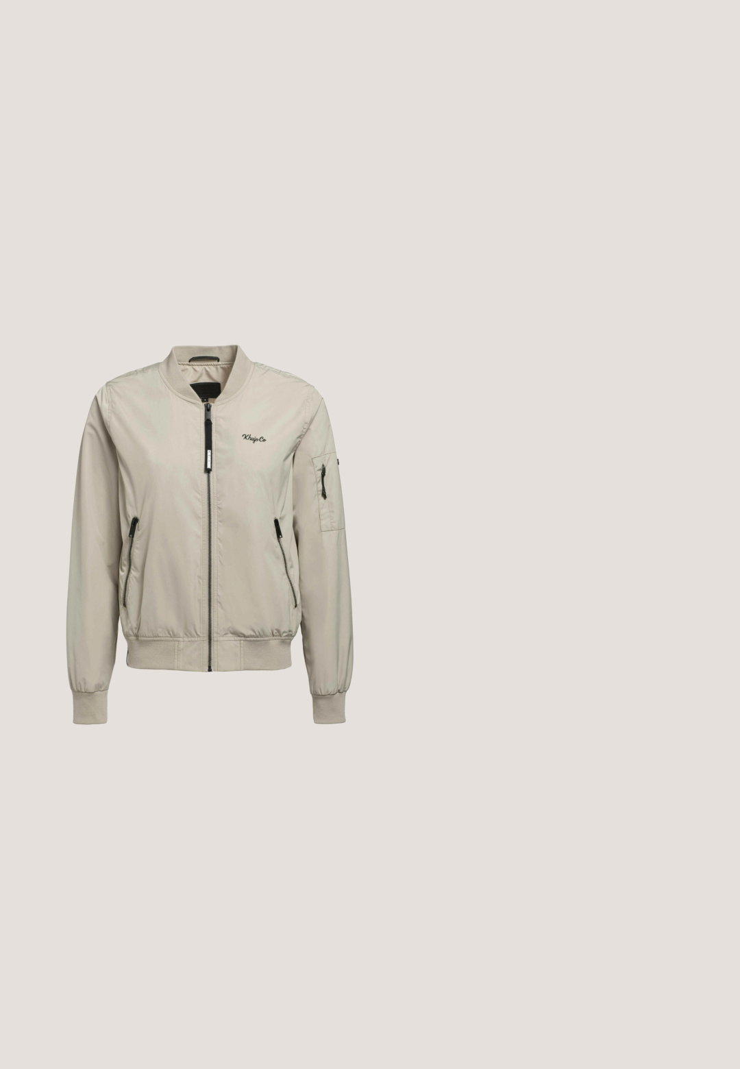 Veste bomber beige avec fermeture éclair à l'avant, deux poches latérales et une poche supplémentaire sur la manche gauche. Elle possède des poignets et un col côtelés.; Sweat-shirt à capuche beige en tissu doux, avec un zip avant demi-longueur, des cordons de serrage et des poignets et un ourlet côtelés. Texture lisse avec un minimum de détails.; T-shirt en coton gris à manches courtes avec un graphique de sardine imprimé et le texte "Niedliche Sardelle" en noir.; Shorts décontractés beiges unis avec une ceinture élastique et des coutures latérales courbées, présentés de face sur un fond blanc.; Baskets légères avec une tige en mesh beige, des accents blancs et des détails texturés en tan. Semelle en caoutchouc épaisse avec un motif ondulé unique.; Sac bandoulière beige avec fermeture éclair, en tissu, design plat, écusson rond avec logo et breloque décorative attachée à la sangle.