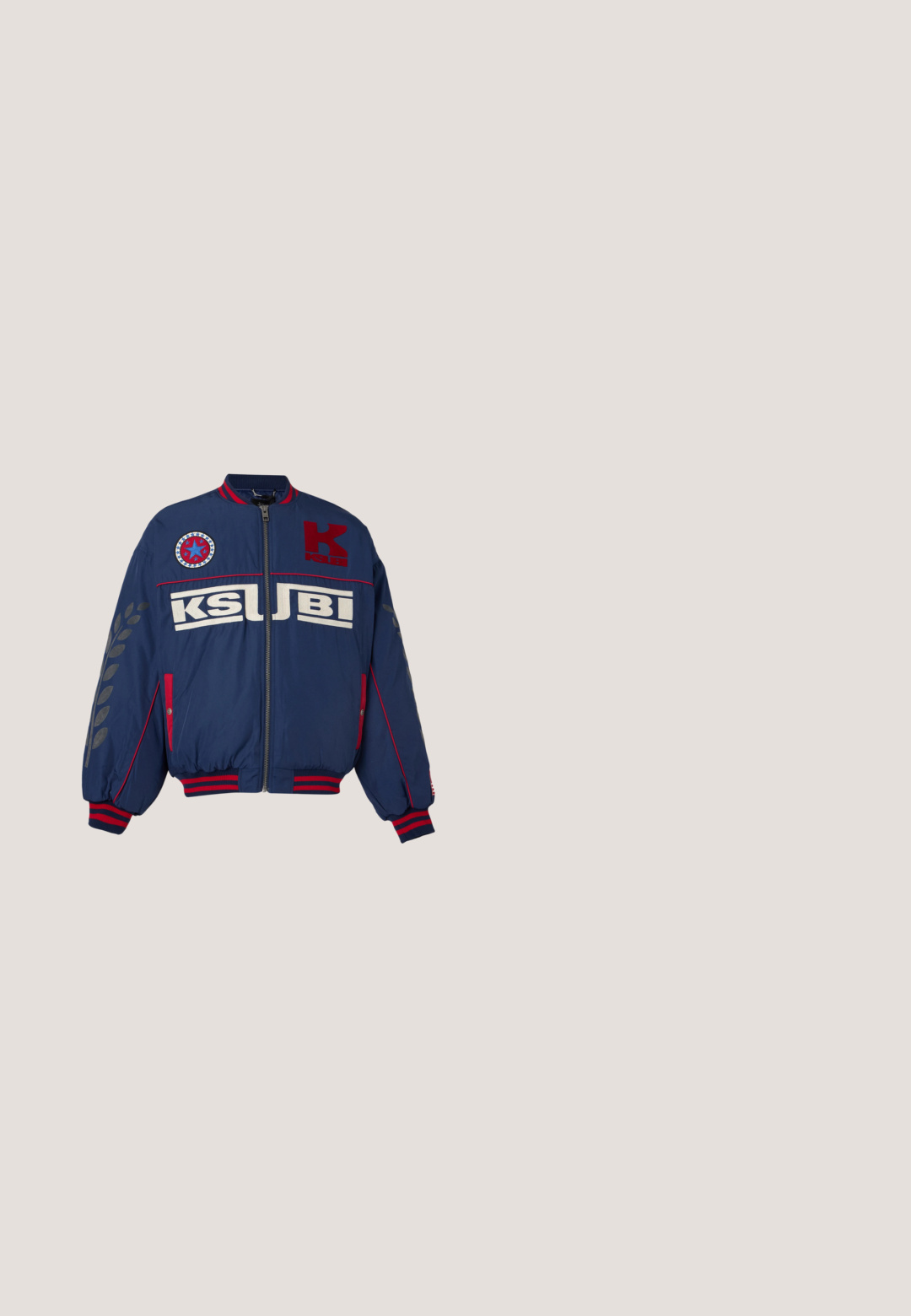 Nachtblauwe bomberjack met rode accenten, rits aan de voorkant, KSUBI-logo tekst op de borst, sterpatch boven links en zwarte bladrandprints op de mouwen.; Witte mesh-shirt met lange mouwen, rode kraag en manchetten, rode en blauwe strepen, grote "TC" tekst en grafische motieven op mouwen en borst.; Marineblauwe mesh korte broek met rode zijpanelen. Voorzien van een elastische tailleband en een trekkoord. Inclusief geborduurd logo op de linker dij.; Zwarte waterdichte rubberlaars met een verstelbare gesp, een gestructureerd oppervlak, een licht gebogen vorm en een robuust profiel voor grip.; Gucci zonnebril met een rechthoekig montuur, zwarte metalen armen, lichtblauwe getinte lenzen en een subtiel G-patroon op de lenzen.; Zwarte canvas tote bag met twee handvatten, een voorvak en "LES DEUX" in blauw geborduurd op het voorvak.