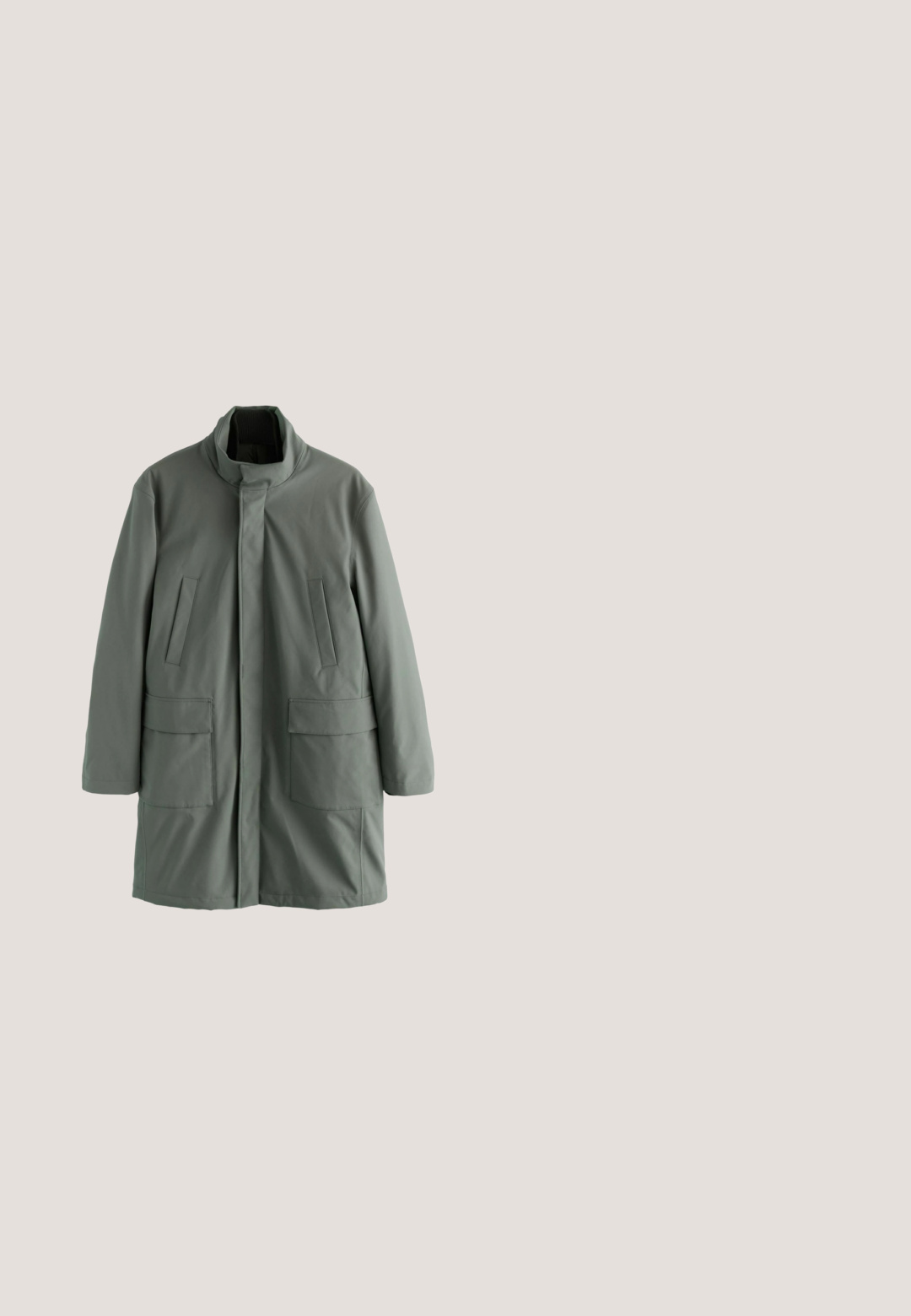 Groene, lichte jas met een hoge kraag, voorzien van twee voorkeurszakken en een gladde, matte textuur. Eenvoudig, recht gesneden ontwerp.; Groene geribbelde trui met een hoge kraag en een rits tot halverwege, met lange mouwen en een structuurbreipatroon.; Donkergroene polo met korte mouwen, voorzien van zwarte kraagaccenten, een rits aan de voorkant en een klein vierkant logo-opdruk op de linkerkant van de borst.; Man draagt grijze slim-fit jeans, witte sneakers met zwarte strepen en een donkerblauw shirt met korte mouwen, staand met één hand in de zak.; Bruine leren enkellaars met suède accenten, ronde neus, vetersluiting, rubberen zool met profielpatroon en een gevoerde kraag voor comfort.; Compact zwart leren crossbodytasje met voorvak met ritssluiting en verstelbare band op een effen witte achtergrond.
