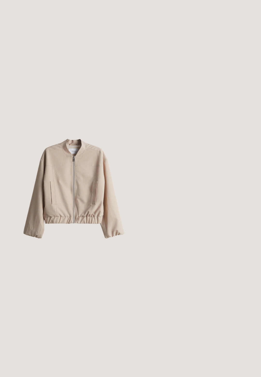 Beige Bomberjacke mit hohem Kragen, Reißverschluss vorne, elastischem Bund und Seitentaschen. Hergestellt aus glattem Stoff mit einem schlichten Design.; Kurzärmliges, hellbeiges Oberteil aus weichem Stoff, mit weitem Ausschnitt und herabgesetzten Schulternähten, in lässiger Passform und minimalistischem Design.; Hellbeige weit geschnittene Hose mit Vordertaschen, Knopf- und Kordelbund sowie umgeschlagenen Säumen.; Hellbeige Slipper mit einem glatten Lederoberteil, weißer Gummisohle und sichtbaren Steppnähten entlang des Umfangs.; Beige weiche Leder-Schultertasche mit verstellbarem Träger und dezentem Branding auf der Vorderseite, vor weißem Hintergrund präsentiert.; Goldfarbener Armreif mit glatter Oberfläche, rundem Verschluss und minimalistischem Design mit gravierten Akzenten.