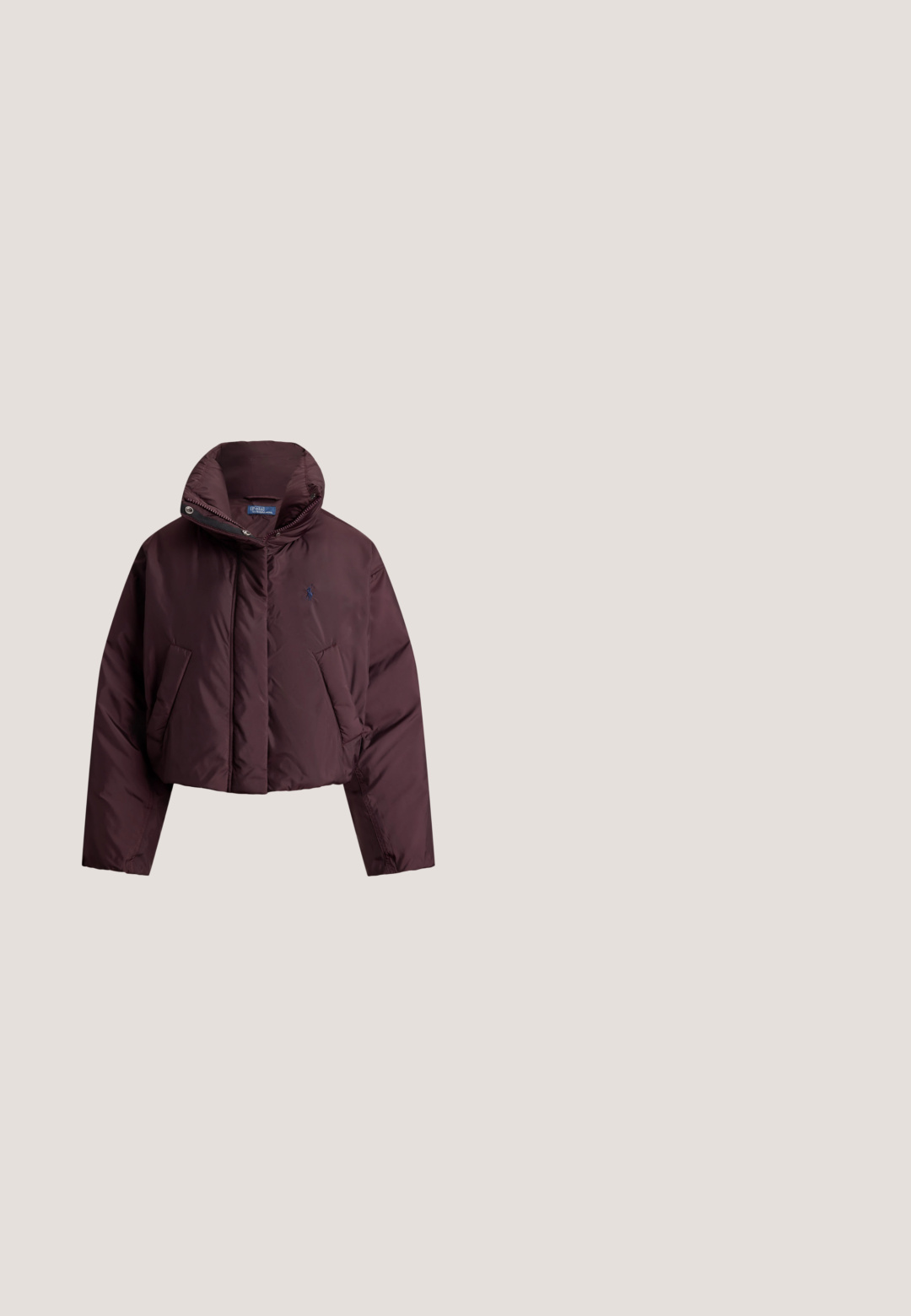 Mørkelilla kort dunjakke med høj krave, sidelommer, frontlynlås og Polo Ralph Lauren-logo på brystet.; Lyserød kabelstrikket langærmet sweater med rund hals og lille blåt broderet logo på brystet.; Lyserød skjorte med lange ærmer, knapper og krave samt blå broderet logo på venstre bryst, vist på ensfarvet hvid baggrund.; Lyserøde joggingbukser i blødt stof med elastik i taljen og snøre samt sidelommer. Diskret logoaccent på låret.; Lavtop rosa ruskind sneaker med brun gummisål og snørebånd, med et lille guldfarvet RLL-logo på sidepanelet.; Grøn lærredstaske med læderdetaljer, to håndtag og en forlomme. Indeholder syningsdetaljer og et diskret logo.