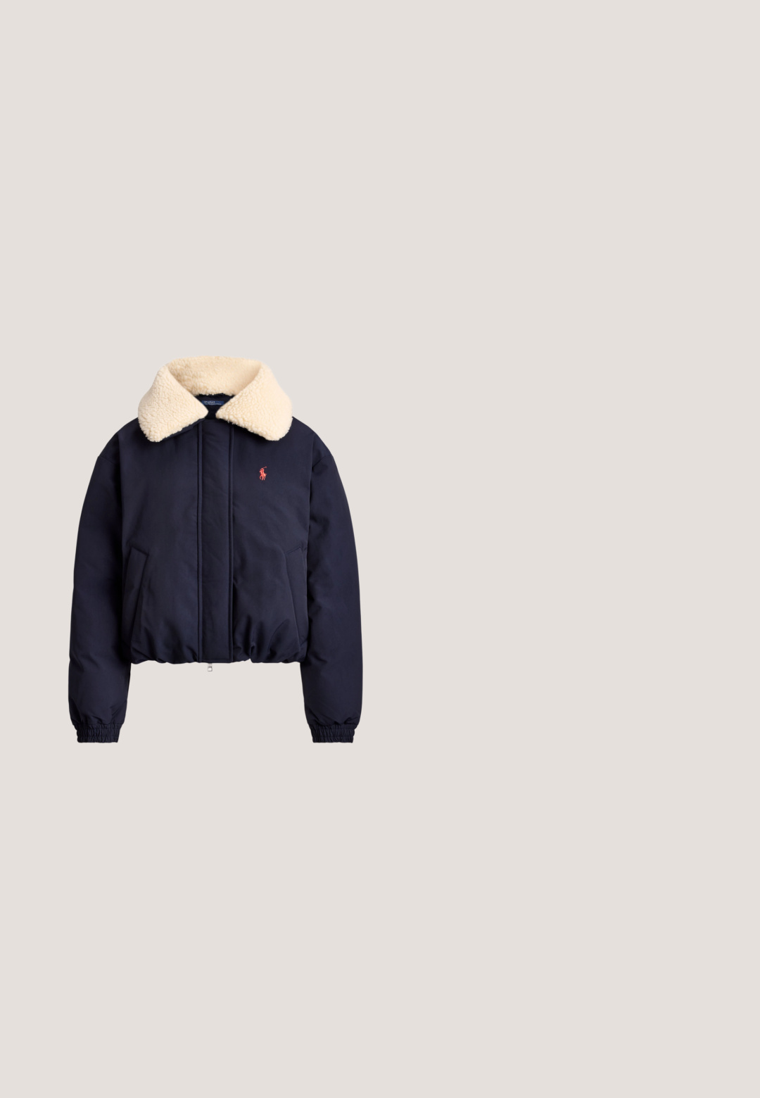 Marineblauw jack met crèmekleurige sherpa kraag, ritssluiting aan de voorkant, zijzakken, elastische boorden en klein rood geborduurd logo op de linkerborst.; Witte coltrui met lange mouwen en een klein donkerblauw geborduurd logo op de linkerborst.; Rugbyshirt met lange mouwen met groene en gele verticale strepen, een groene kraag en het geborduurde Polo Ralph Lauren-logo met een rode roos.; Donkerblauwe denim jeans met een rechte pasvorm, voorzien van oranje stiksels, een sluiting met knoop aan de voorkant en vijf zakken.; Lage casual sneaker in beige suède met groene en blauwe accenten, witte veters, rubberen zool en bruine hielstrook.; Bruine suedé handtas met een gebogen vorm, gouden hardware en een ritsluiting. Voorzien van een korte, verstelbare schouderriem.