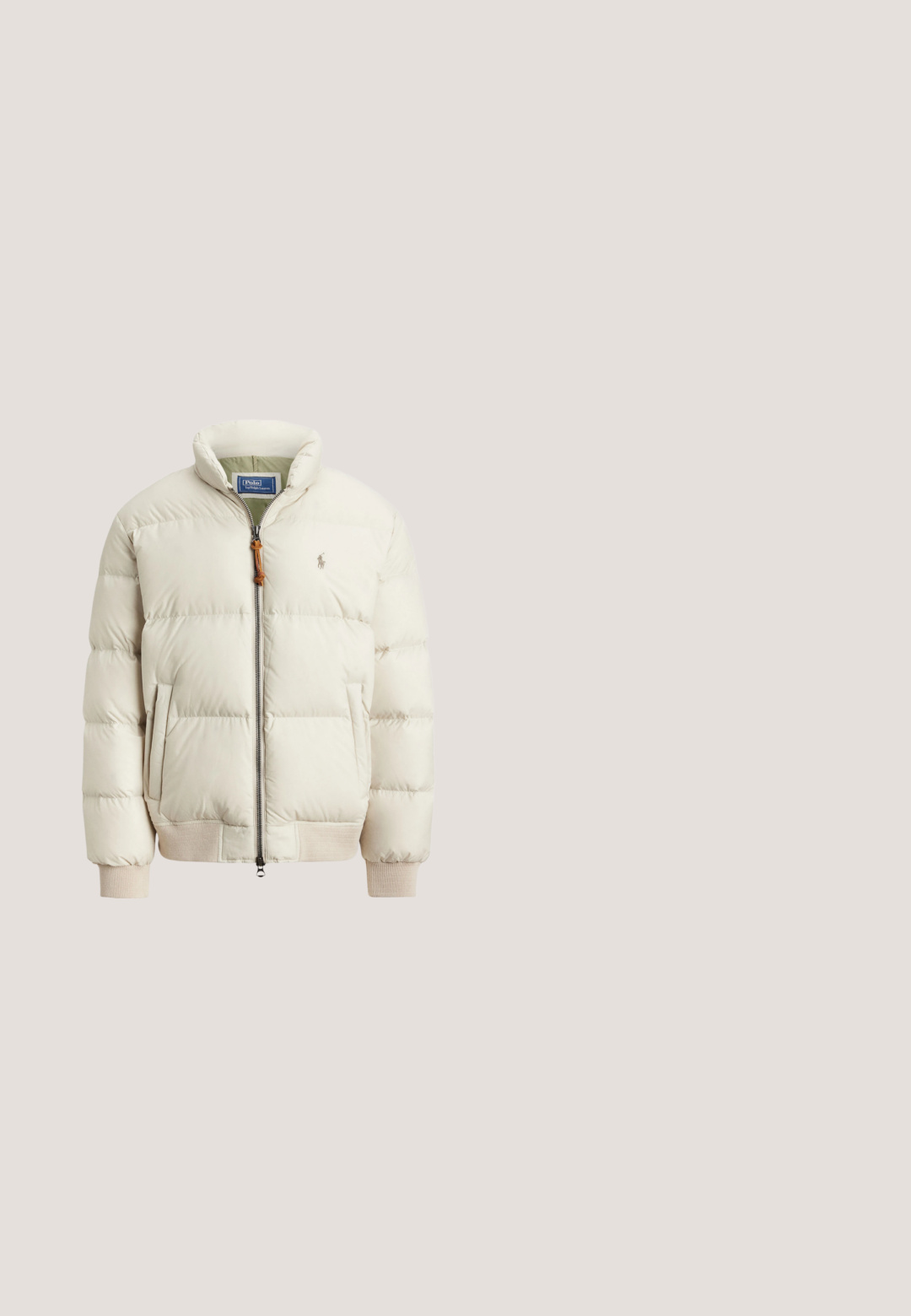 Chaqueta tipo puff en beige claro con cierre frontal, puños acanalados y bolsillos laterales. Presenta un pequeño logo en el pecho y un acabado texturizado.; Jersey de punto de manga larga color crema con cremallera frontal hasta la mitad, cuello, puños y dobladillo acanalados, con un pequeño logo Polo oscuro en el pecho.; Polo color crema con el texto Ralph Lauren, logo bordado del jugador de polo, número 3 en la manga y escudo con corona en el pecho.; Pantalones deportivos beige con cordón, bolsillos laterales y logo y emblema rojo "POLO" en la parte superior del muslo izquierdo.; Vista lateral de zapatilla beige y marrón con detalles en ante y logo Polo en el lateral sobre un fondo liso.; Cinturón tejido verde oliva con hebilla metálica plateada y presilla y extremo de cuero marrón con el logotipo en relieve de un caballo y jinete.