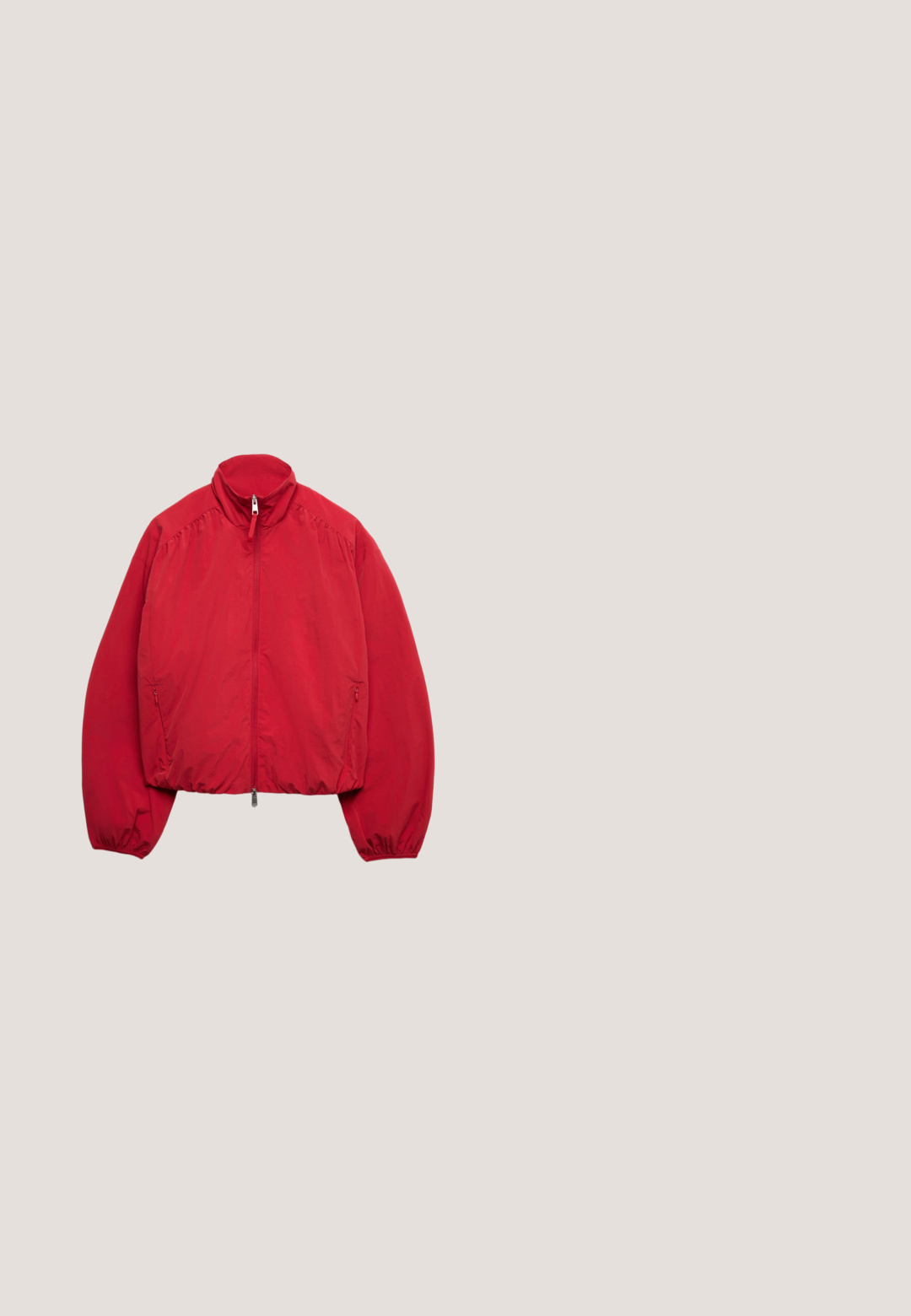 Chaqueta ligera roja con cremallera completa en la parte delantera, cuello alto, puños elásticos y bolsillos laterales con cremallera, colocada plana sobre un fondo blanco.; Suéter de punto rojo con escote en V, que presenta un diseño de calado, acentos de rayas blancas en el escote y los puños, y mangas largas.; Camiseta roja de manga corta con estampado blanco en el pecho que dice "CLUB D'ÉTÉ" junto a elementos gráficos de olas y cuadrados.; Pantalones deportivos rojos con un diseño de pierna ancha, que cuentan con una cinturilla elástica y franjas blancas a los lados. Fabricados con un material suave y ligero.; Zapatilla deportiva de ante rojo con un detalle dorado en el talón, que presenta un diseño texturizado y una suela de goma color caucho, asegurada con cordones planos.; Bolso bandolera rectangular de cuero rojo con bolsillo delantero y cremallera plateada, con la marca "Trussardi" en letras pequeñas blancas.