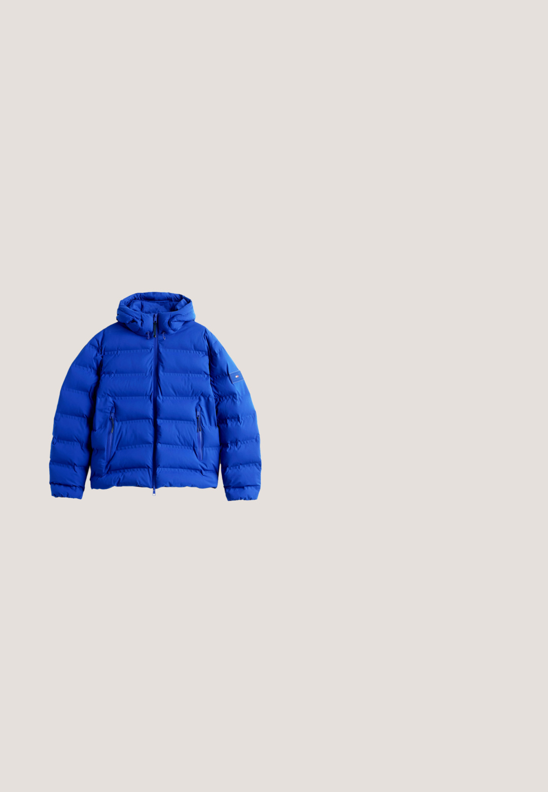 Blå pufferjakke med hætte, med horisontale quiltede sektioner, to lynlåsede sidelommer og et logo patch på ærmet.; Lyseblå langærmet trøje med rund hals, ribkant ved ærmer og kant, med et lille Tommy Hilfiger flaglogo på brystet.; Lyseblå skjorte med lange ærmer, knapper og krave samt et lille rektangulært logo på venstre bryst, lagt fladt på en hvid baggrund.; Blå denimjeans med lige snit, der har fem lommer, knaplukning og let falmning over stoffet for tekstur.; Brune ruskinds Chelsea støvle med elastiske sidepaneler, rund tå og en lille strop bagpå; sort gummisål med subtil tekstur.; Sort læder toilettaske med struktureret finish, lynlåslukning, logo-patch og lille rød, hvid og blå accentstribe.