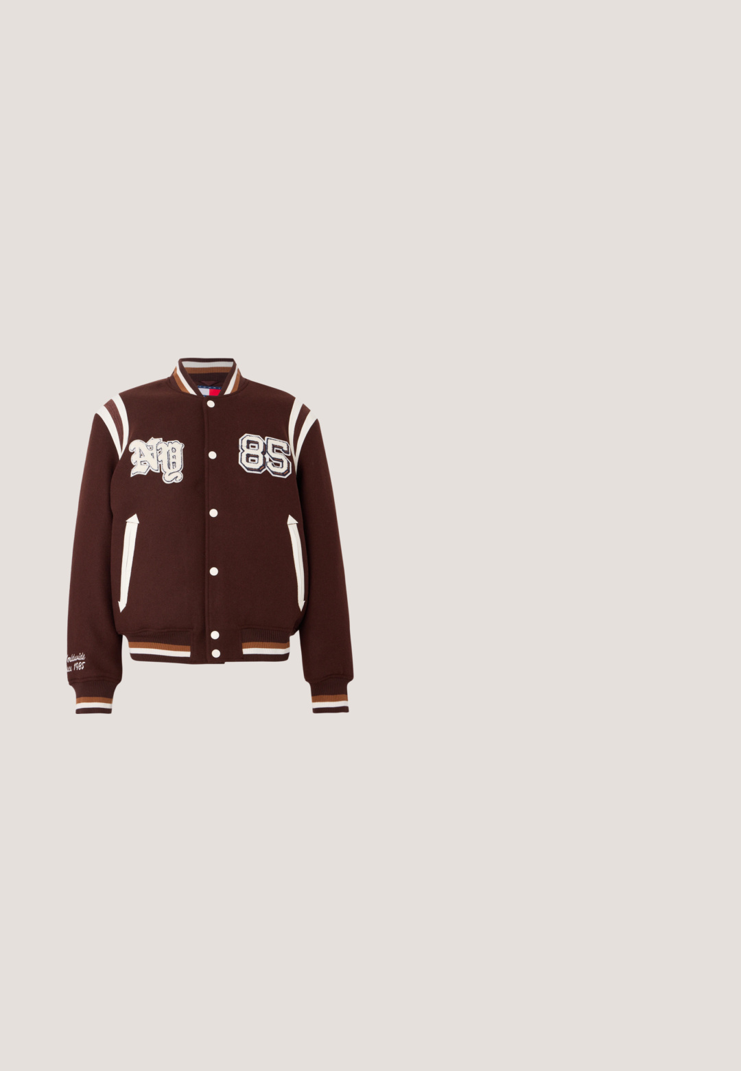 Brun varsityjakke lavet af uldblandinger, med hvide striber, broderede nummer "NY" og "85," samt ribbede manchetter med farvede accenter.; Cremefarvet striktrøje med et markant rødt og marineblåt logo med ordene "TOMMY JEANS" og "NYC 1985." Ribbestrikkede manchetter og kant.; Lyse beige bomulds T-shirt med korte ærmer, rund hals og "TOMMY JEANS" logo i sort på tværs af brystet med et lille rødt og blåt emblem.; Lyseblå denimjeans med lige ben, der har en knap- og lynlås lukning, fem lomme-stil og subtilt slid.; Sneakers i cremet beige ruskind med marineblå striber, hvide snørebånd og en brun gummisål. Logoet vises på siden og hælen.; Crossbody taske i tanfarvet stof med rektangulær form, forreste lynlåslomme og et mærkepatch. Har en justerbar rem og syningsdetaljer.