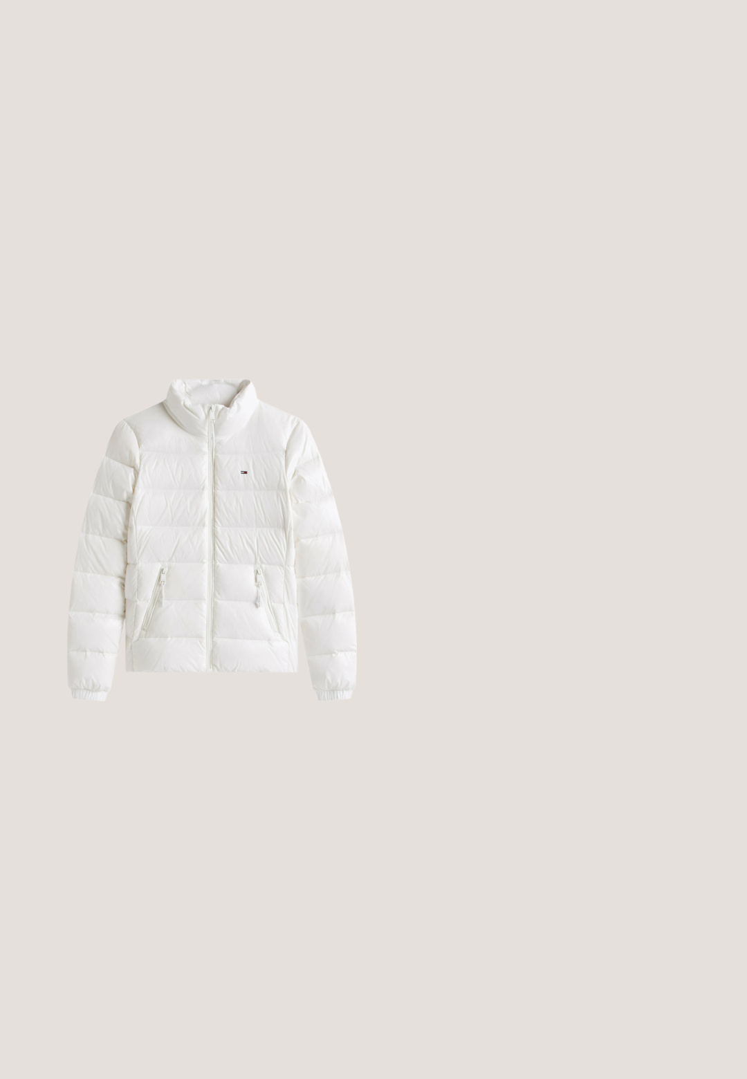 Weiße Pufferjacke mit Reißverschluss, hohem Kragen, zwei vorderen Reißverschlusstaschen und elastischen Bündchen. Verfügt über horizontale Steppung für Wärme.; Blauer Strickpullover mit Reißverschlusskragen, mit Rautenmuster und gerippten Bündchen und Saum. Mit einem aufgestickten Logo auf der Vorderseite.; Weißes ärmelloses, geripptes Tanktop mit dem Schriftzug „tommy jeans“ und rotem Stern auf der Brust, kleinem Tommy Hilfiger Flaggenlogo am Saum.; Helleblaue Jeans mit hoher Taille, Frontknopf und Reißverschluss, fünf Taschen und leicht ausstellenden Beinen.; Schwarzer Knöchelstiefel mit elastischer Seitenpartie, schwebend über Holzquadratischfliesen mit Kies in einem Außenbereich.; Schwarze Handtasche aus synthetischem Leder mit geschwungener Form, verstellbarem Schulterriemen und silbernem Reißverschluss. Mit kleinem Logo am unteren Rand.