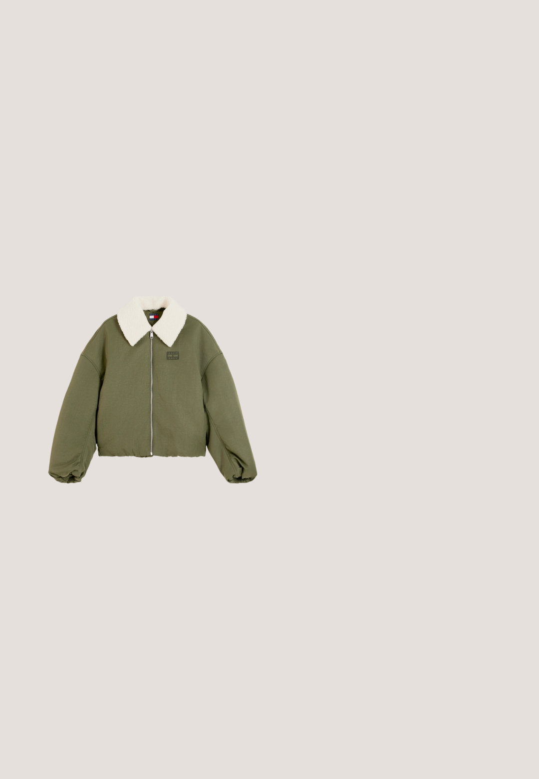 Veste courte vert olive avec manches oversize, col en polaire blanc, fermeture éclair frontale et poignets élastiques.; T-shirt en coton rouge avec un imprimé logo blanc indiquant "TOMMY HILFIGER CO." sur le devant, avec un col rond et des manches courtes.; Jean à jambes larges en denim bleu clair. Il présente une taille haute, deux poches avant, un léger délavage sur les cuisses et un ourlet droit.; Baskets basses noires avec un col rembourré blanc, lacets noirs, semelle marron et un petit logo métallique sur le panneau latéral.; Sac à main synthétique rouge et brillant avec une longue bandoulière réglable et une fermeture éclair. Présente un logo gravé discret sur un côté.; Bracelet en argent avec un fermoir en forme de cœur, affichant un design à double chaîne, une gravure de logo et un détail d'accent en rouge, blanc et bleu.