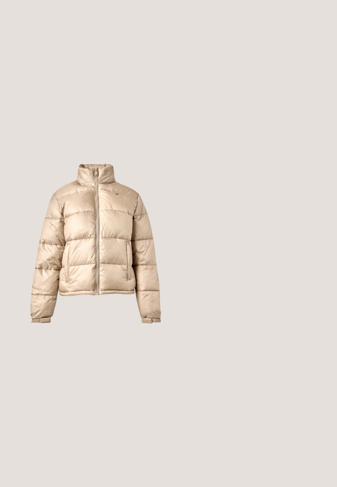 Beige gewatteerd jack met horizontale doorgestikte lijnen, ritssluiting aan de voorkant, opstaande kraag en twee zijzakken, afgebeeld op een lichtgrijze achtergrond.; Wit katoenen T-shirt met korte mouwen en een ronde hals, met "TOMMY HILFIGER" in dikke rode letters. Opvallend grafisch ontwerp.; Wijdvallende donkerblauwe spijkerbroek van denim, met een rits, knoopsluiting en twee voorzakken met contrasterende stiksels.; Witte lage sneaker met gouden oogjes, goud logo op de zijkant en gouden accent op de hiel, weergegeven tegen een plain witte achtergrond.; Marineblauwe leren clutch met een goudkleurige kettingband en een sluiting aan de voorkant. Heeft een gladde textuur en een hoekig ontwerp.; Goudkleurige hartvormige oorbellen met uitsparing in het midden, gestructureerd oppervlak en gegraveerd logo-detail. Veilige post-back sluiting.