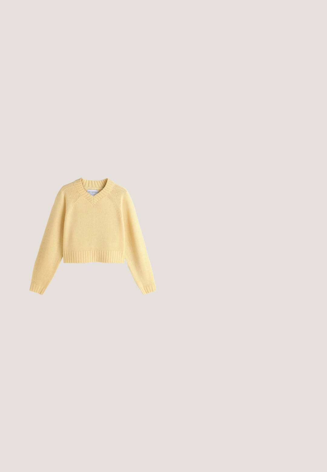 Suéter corto amarillo hecho de 100% lana de cordero, con cuello en V, puños y dobladillo acanalados, y detalle de tejido texturizado en las mangas.; Camisa beige de botones con cuello, mangas largas y dos bolsillos en el pecho. Presenta un logo bordado y una textura suave y lisa.; Vaqueros de pierna ancha en un tono azul claro, fabricados en denim, con una cintura de altura media, dos bolsillos frontales y detalles de costura clásica.; Zapatilla baja de color beige con tejido de malla y superposiciones de ante, suela de goma y diseño con cordones sobre fondo blanco.; Bolso de hombro de cuero beige con correa ajustable y cierre de cremallera, presentado sobre un fondo beige claro.; Cadena de metal en tono dorado con un diseño retorcido. Presenta un cierre de garra y eslabones alargados, dispuestos en una disposición fluida y curva.