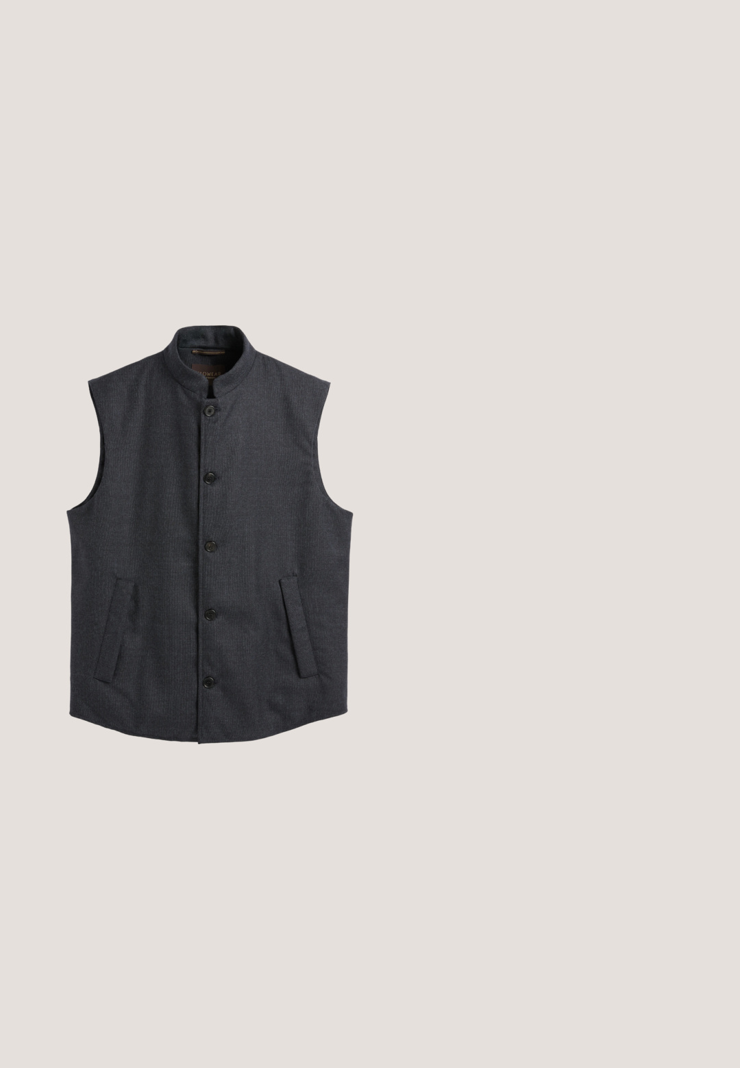 Donkergrijze mouwloze bodywarmer met hoge kraag, vijf knopen aan de voorkant en twee schuin geplaatste zijzakken, plat gelegd op een witte achtergrond.; Navyblauwe v-hals trui gemaakt van zacht breimateriaal met lange mouwen en geribbelde boorden, met een gladde textuur en minimale details.; Marine knoopshirt gemaakt van textuurstof, met een puntige kraag, lange mouwen en een klein geborduurd ontwerp op de linkerborst.; Donkerblauwe formele broek met knoop- en ritssluiting, riemlussen, steekzakken en een rechte pijp op een witte achtergrond.; Zwarte suède instapschoen met beige zool, ronde neus en minimale stikdetails op een effen witte achtergrond.; Compacte marineblauwe pebbled leren schoudertas met ritscompartimenten en zilveren Lancaster-logo op het voorpaneel.