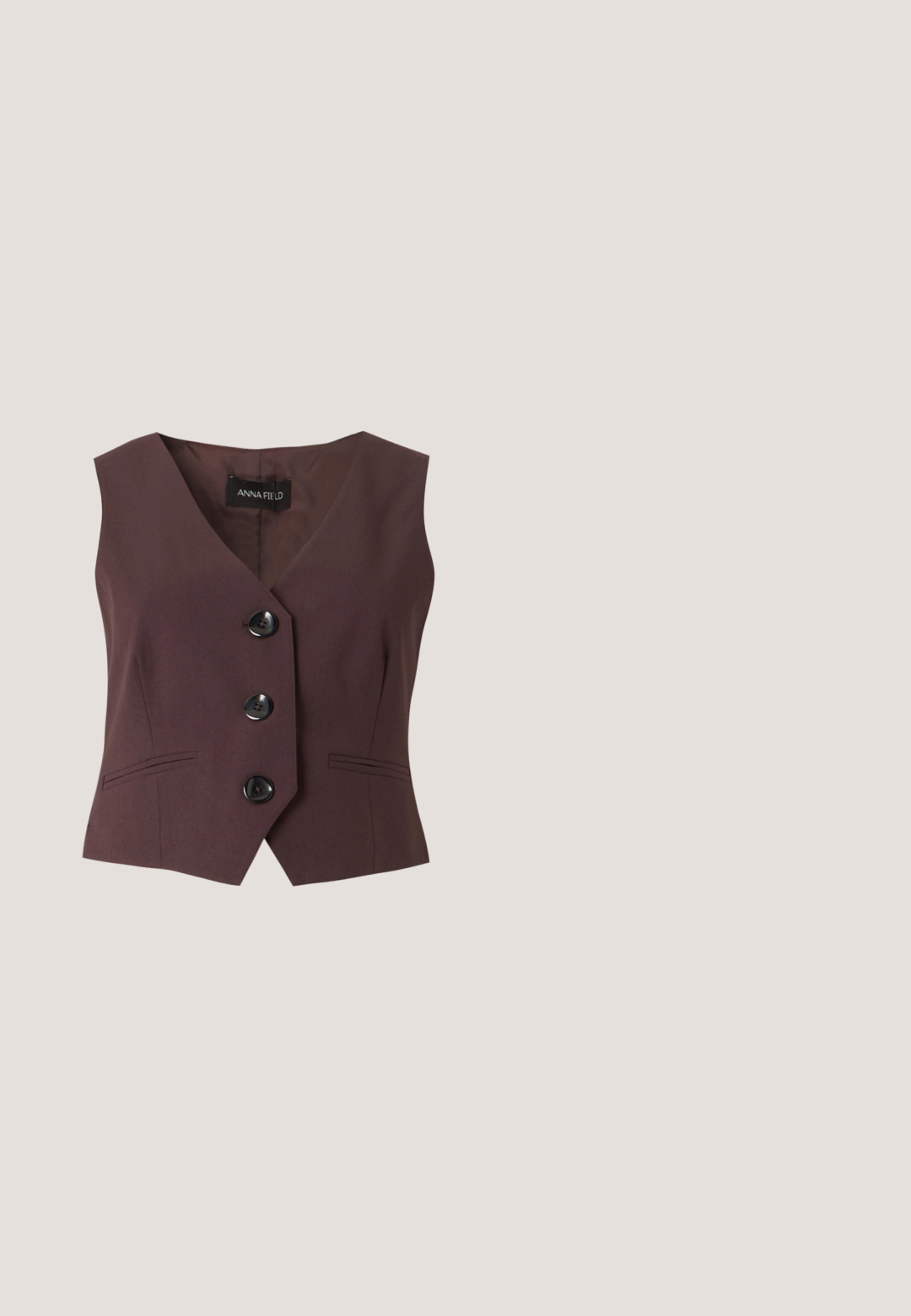 Gilet sans manches marron foncé avec col en V, trois grands boutons noirs et deux poches avant fines, étiqueté Anna Field.; Chemise marron foncé à manches longues avec boutons, col, taille à cordon et larges poignets, présentée sur un fond neutre.; Pantalon noir taillé avec une texture lisse, présentant une coupe droite, des passants pour ceinture et deux plis avant pour plus de détails.; Chaussure à talon haut en cuir marron avec bout pointu, trois petites boucles argentées sur le devant et bride de cheville réglable avec boucle.; Sac à main bordeaux en matériau brillant, de forme rectangulaire, avec deux anses et des accents légèrement courbés à l'avant.; Paire de boucles d’oreilles créoles en or irrégulières et asymétriques avec une finition lisse et mate sur un fond neutre.