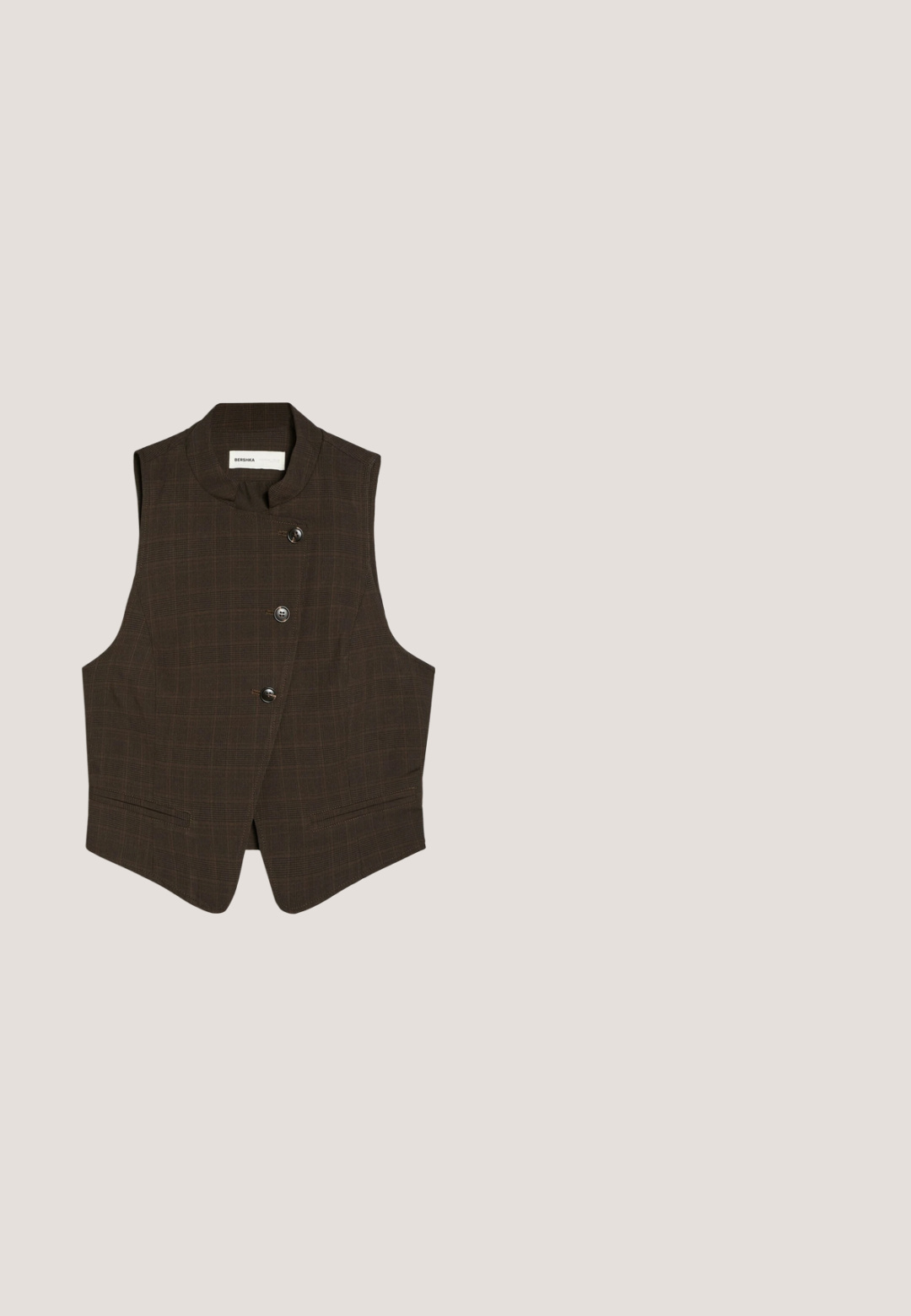 Gilet sans manches marron foncé avec col montant et trois boutons sur le devant, avec un motif à carreaux subtil et deux poches avant.; Chemise blanche à manches longues avec col classique et fermeture boutonnée à l'avant ; elle est conçue dans un tissu léger et lisse avec un ourlet arrondi.; Pantalon à jambes larges en tissu marron foncé, avec plis à l'avant et texture lisse. Pas de poches visibles ni d'ornements.; Mule marron foncé à bout ouvert, talon bas incurvé et large bride sur l'avant.; Lunettes de soleil teintées marron avec une monture en écaille de tortue. Présentent une forme en œil de chat angulaire et des accents jaunes embellis sur les branches.; Sac à main en cuir marron avec deux poignées, une sangle centrale à boucle et des ferrures dorées, présenté sur fond blanc.
