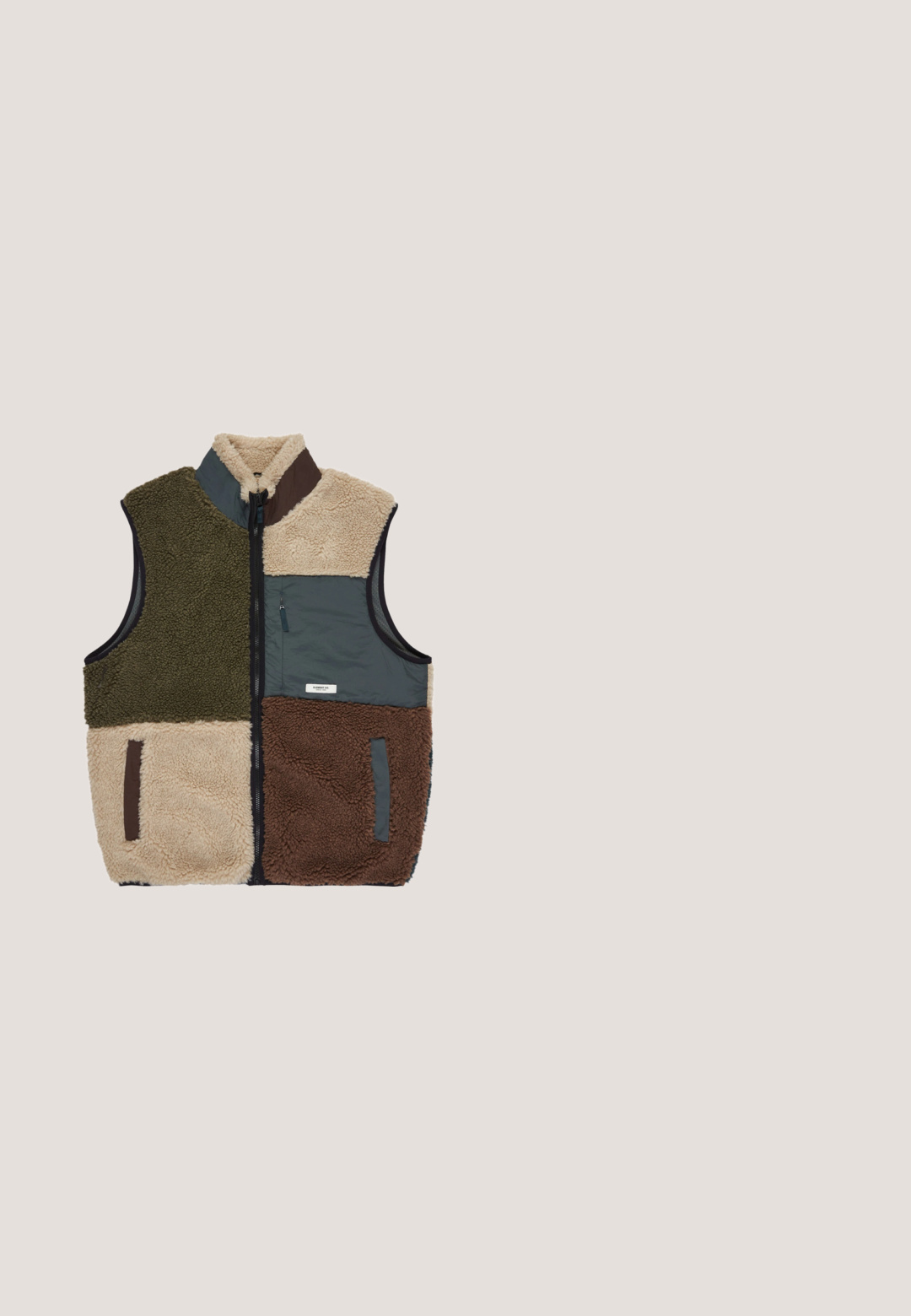 Fleece-Weste mit hohem Kragen, bestehend aus grünen, beigen, grauen und braunen Paneelen. Mit Reißverschlusstasche auf der Vorderseite, strukturierter Stoff im gesamten Design.; Helles blaues Sweatshirt aus weichem Stoff, mit Rundhalsausschnitt und langen Ärmeln. Kleines schwarzes "VANS"-Logo auf der Brust. Lässiger Schnitt.; Kurzärmeliges T-Shirt mit Rundhalsausschnitt, dünne horizontale braune und hellgrüne Streifen, mit kleinem Vans-Logo auf der Brust.; Khaikifarbene Baumwollhose mit geradem Bein, ausgestattet mit zwei großen Fronttaschen und einer seitlichen Tasche, abgeschlossen mit einem Knopfverschluss.; Grüne Wildledersneaker mit strukturiertem Finish, kontrastierenden sandfarbenen Akzenten an der Ferse und einer cremefarbenen Gummisohle. Schwarze Schnürsenkel und gestickte Details.; Grüne Umhängetasche aus strapazierfähigem Stoff, mit einer Front-Reißverschlusstasche, einem schwarzen Tragegurt und einem horizontalen weißen Akzentgurt.