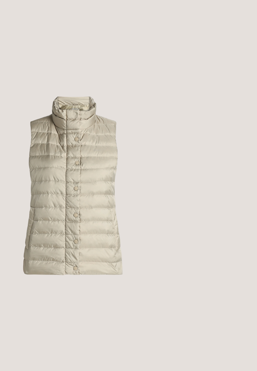 Veste matelassée beige sans manches avec un col montant et une fermeture pressionnée à l’avant, présentée à plat sur un fond blanc.; T-shirt à manches courtes couleur pêche claire avec encolure ronde et petite poche poitrine, présenté sur un fond uni.; Jean droit avec des panneaux avant noirs et des panneaux latéraux bleus, avec poches avant et fermeture par bouton.; Bottines Chelsea en daim marron avec des panneaux élastiques sur les côtés, une languette de tirage, une semelle en caoutchouc et une surface texturée, dotées d'un bout arrondi et d'une conception robuste.; Sac à épaule en daim marron avec une bandoulière unique, un haut incurvé et un petit pompon avec un charme doré sur le côté, sur un fond uni.; Boucles d'oreilles créoles texturées en ton or, dans une forme organique avec un léger éclat et une fermeture arrière sécurisée.