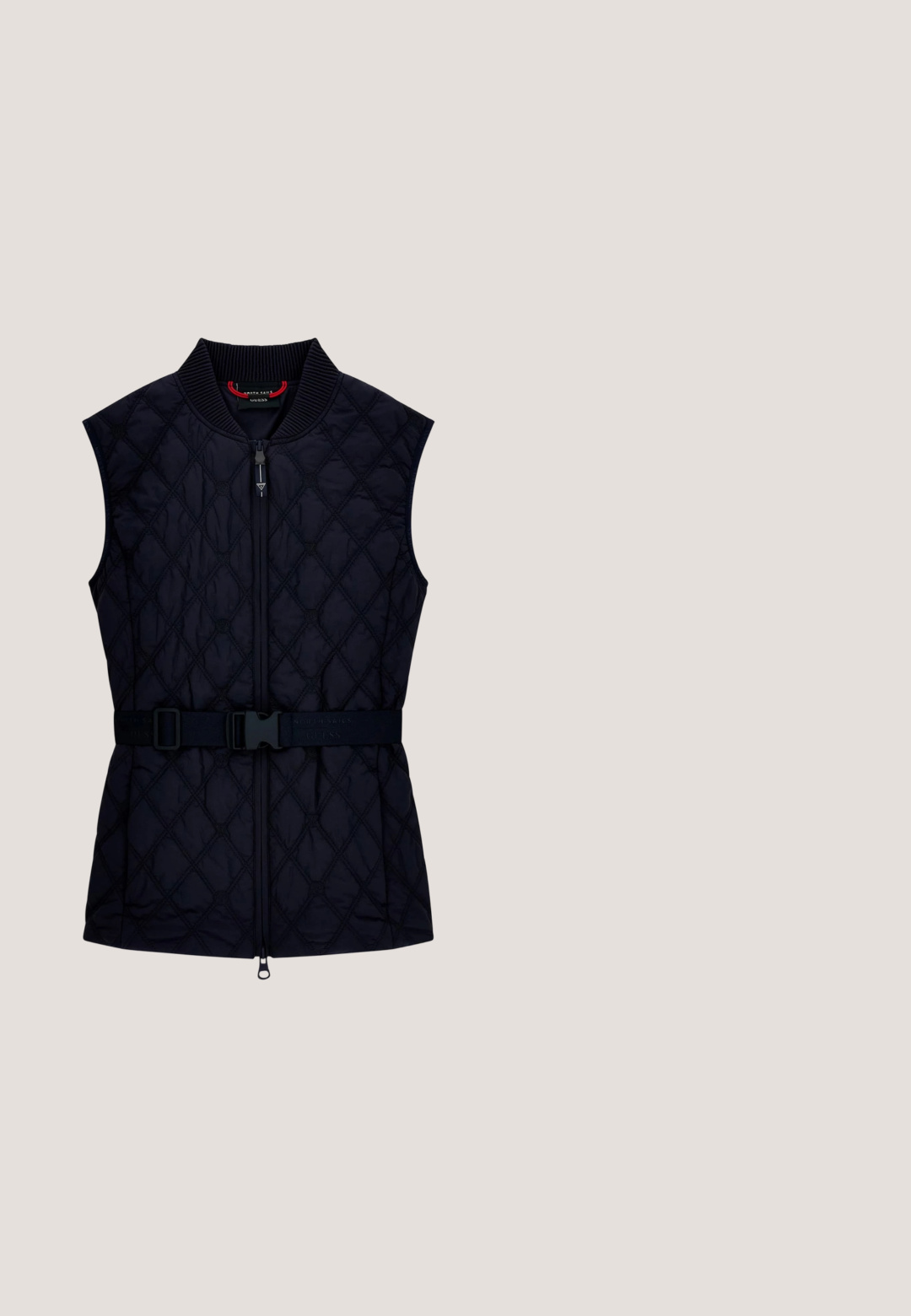 Chaleco negro acolchado sin mangas con cremallera frontal, cuello acanalado y cinturón ajustable con hebilla en la cintura.; Camiseta de algodón azul marino con mangas cortas, que presenta un pequeño logo blanco de "Calvin Klein" en el centro frontal. Cuello redondo, ajuste casual.; Jeans ajustados de mezclilla azul medio, con cintura alta, textura suave, dos bolsillos frontales y un solo bolsillo trasero.; Zapatilla negra con materiales mixtos, que presenta un upper texturizado con un patrón sutil, entresuela blanca y un acento metálico en el talón.; Pequeño bolso crossbody rectangular de cuero crema con el logo "cK" en relieve en la parte delantera y correa ajustable.; Par de pendientes de aro de oro pulido con forma irregular y cierre de botón, sobre un fondo blanco liso.
