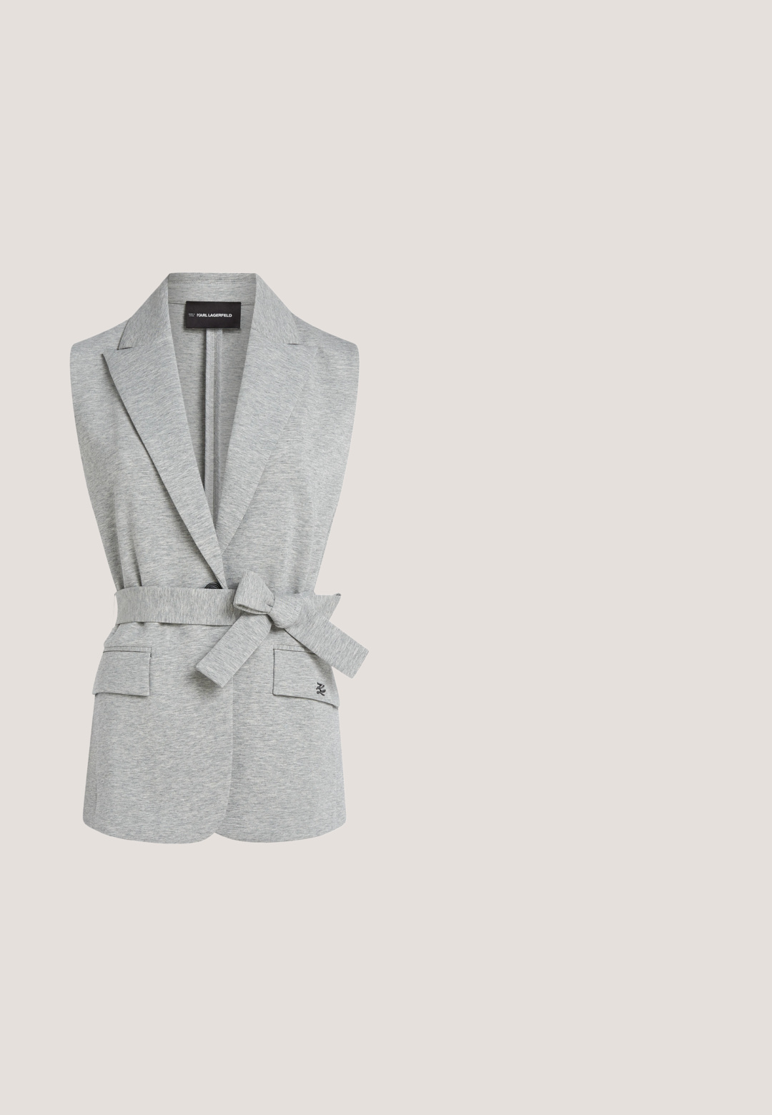 Grå ærmeløs blazer med bælte, to forlommer og en blød tekstur. Har en spids slå-om og minimalistisk design.; Grå langærmet sweater med en asymmetrisk halsudskæring. Lavet af et blødt, struktureret materiale. Har en lille logo detalje nær kraven.; Sorte bukser med en glat stofkvalitet, lige ben-design og elastisk talje. Inkluderer lodrette sømdetaljer.; Sorte læder loafers med en glat overflade, med en guldfarvet hardware detalje på vampen og en lav, flad sål.; Sort rektangulær skuldertaske i læder med sølvlynlås og sølv "K"-logo på fronten, vist mod en ensfarvet lys baggrund.; Guldøreringe med en oval gennemsigtig sten i midten. Har en glat, blank overflade og et indgraveret brandlogo på den ene side.