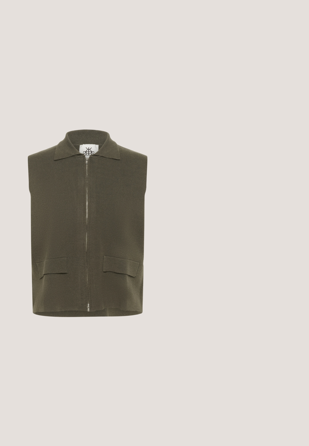Veste sans manches zippée de couleur vert olive, en tissu tricoté texturé. Elle comporte un col plat et deux poches avant.; Pull court beige en tricot doux. Présente des manches courtes, un col rond et une texture subtile. Étiquette visible à l'intérieur du col.; Pantalon large en lin beige avec passants de ceinture et fermeture par bouton à la taille, présenté à plat sur un fond blanc.; Chausson à enfiler en suède marron avec doublure en polaire blanche et semelle en caoutchouc épaisse à fond antidérapant, présenté en vue latérale.; Lunettes de soleil œil de chat en écaille de tortue avec des verres teintés vert foncé et des montures angulaires, présentées sur un fond blanc.; Sac bandoulière en cuir marron foncé avec motif tressé, fermeture à rabat et large sangle assortie, posé sur un fond blanc uni.