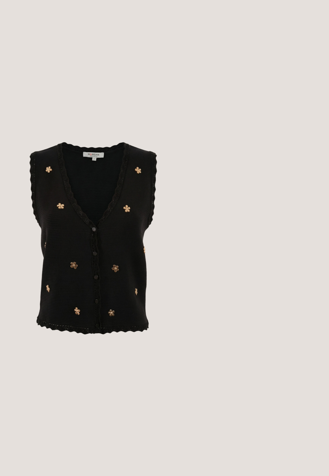 Chaleco de punto negro sin mangas con bordes ondulados, botones frontales y pequeños adornos dorados en forma de flor distribuidos por el frente.; Blusa negra con escote redondo, mangas abullonadas y detalles decorativos de corte alrededor de los hombros y los puños. Tejido texturizado.; Jeans de mezclilla azul claro con corte recto, de talle alto, con un lazo frontal y diseño clásico de cinco bolsillos. Superficie texturizada con un ligero desvanecimiento.; Sandalia de tacón alto en burdeos de charol con punta abierta, que cuenta con tiras cruzadas y una correa al tobillo con una hebilla redonda dorada. Diseño de tacón cuadrado.; Bolso negro hecho de un material brillante y texturizado con un asa circular retorcida y un cierre de cremallera. Presenta un diseño suave y arrugado.; Pendientes de aro dorado con pétalos de tela roja profunda en capas y dos delicadas cadenas doradas colgando de cada uno.