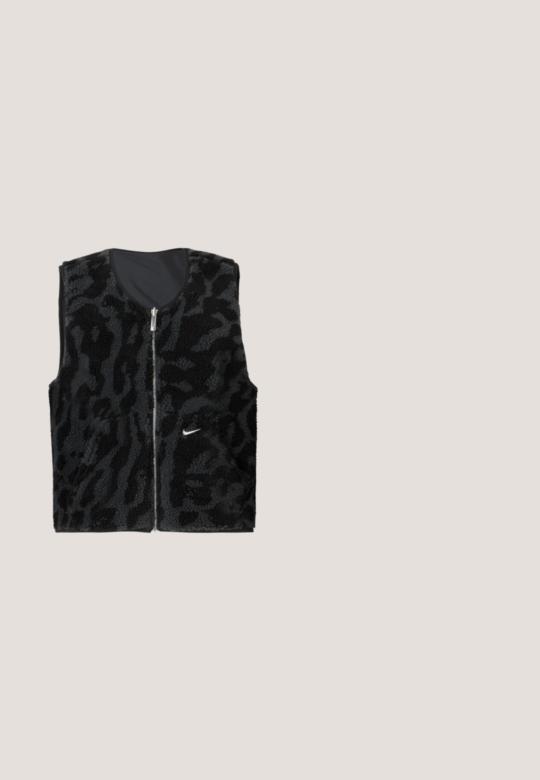 Sort fleece vest med lynlås foran, der har et tekstureret dyreprintdesign og et lille hvidt Nike-logo på venstre side.; Kroppet sweatshirt i lysegrå, lavet af blødt stof. Har rund hals, lange ærmer med elastiske manchetter og et sort Nike-logo over brystet.; Sort Nike T-shirt med korte ærmer, stor hvid "NIKE" tekst, lille guldfarvet Nike swoosh over teksten og "SPORTS CLUB" tekst under logoet.; Sorte sweatpants lavet af blødt stof, med en elastisk talje og snøre, sidestriber og et lille logo på venstre front.; Sort lavtop Nike-sneaker med snørebånd, syet detaljering og en tekstureret sål imod en simpel hvid baggrund.; Sort quiltet tote-bag med polstret tekstur og snørelukning, der har to lange sorte håndtag.