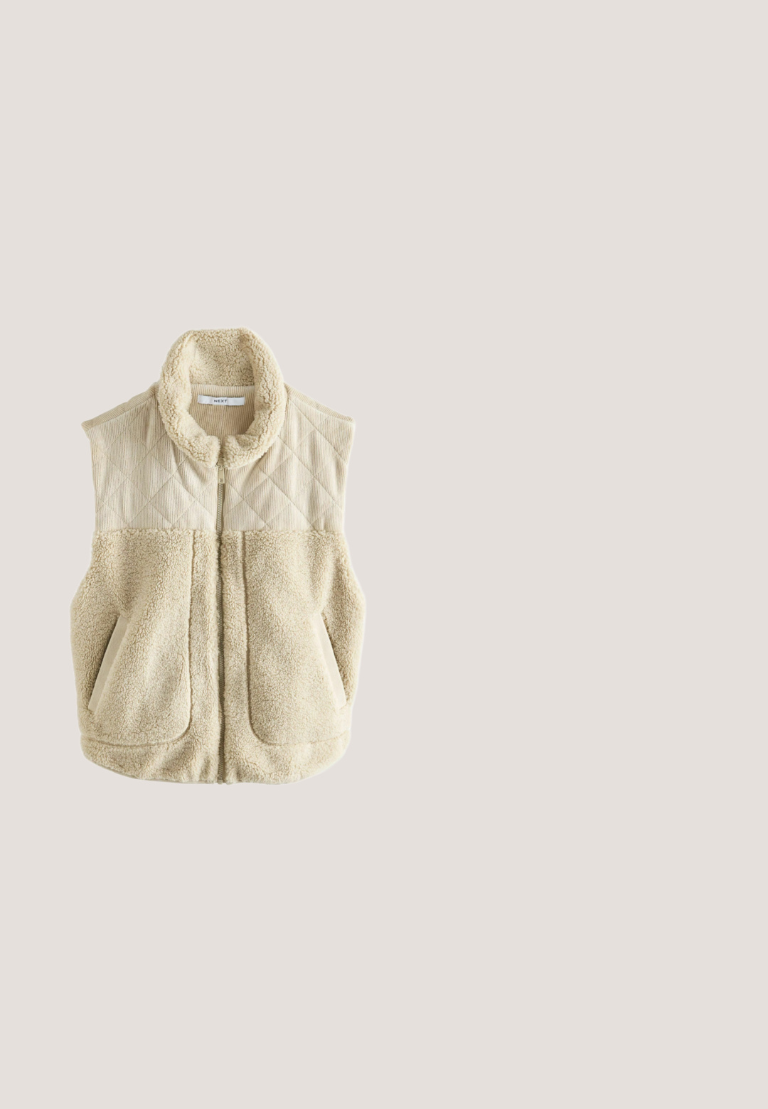 Beige vest met een gearceerde bovenkant van corduroy en een zachte neplederen onderkant. Hoog kraag en twee voorzakken. Ritssluiting in het midden.; Olijfgroene sweatshirt van zachte stof, met een hoge kraag, een half-rits sluiting en verlaagde schouders voor een ontspannen pasvorm.; Beige T-shirt met korte mouwen en een ronde hals in een ontspannen pasvorm op een witte achtergrond.; Licht olijfgroene cargo pants van katoen, met een trekkoord in de taille, twee grote zakken aan de voorkant en taps toelopende benen.; Olijfgroene sneakers met zwarte accenten, gemaakt van suede en mesh materialen, ronde neus en gestructureerde zolen. Gepaard met lichtgrijze denim broek.; Compact olijfgroene crossbodytas met zwarte verstelbare riem, voorvak met ritssluiting en klein logodetail rechtsonder.