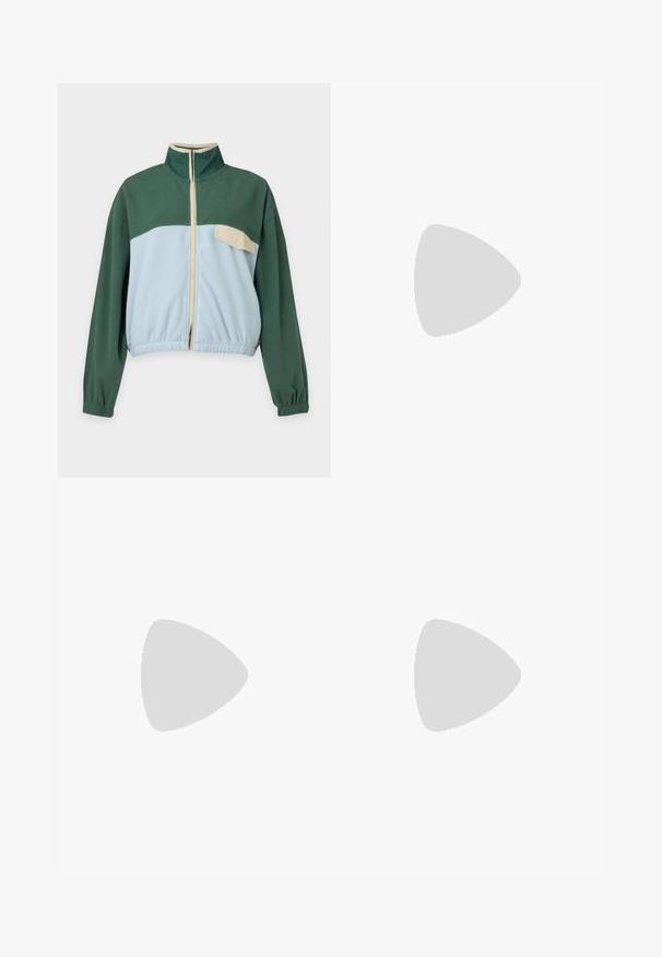 Chaqueta de forro polar verde y azul claro con cremallera frontal, cuello alto, puños elásticos y un bolsillo en el pecho con botón a presión beige en el lado izquierdo.; Top de tirantes de canalé color crema con cuello redondo y sin mangas, que presenta un logotipo bordado de "Santa Cruz" en rosa y azul en la parte frontal.; Falda negra de mezclilla hasta la rodilla con bolsillos frontales, trabillas para cinturón y detalle de costura central.; Zapatilla negra y beige con una correa de velcro, tres rayas blancas en el lateral y una suela de goma marrón texturizada. Logotipo de la marca visible.