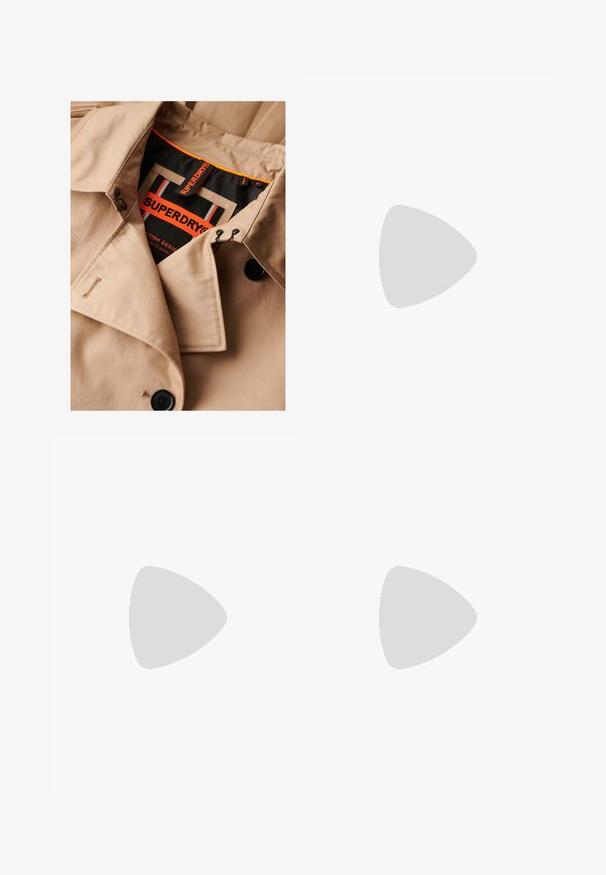 Beige trenchcoat met donkere knopen, dubbele borstsluiting en zwarte kraagvoering. Voorzien van een "SUPERDRY" label in oranje en zwart.; Wit, kort mouw, boxy t-shirt gemaakt van zacht katoen. Heeft een ronde hals en brede mouwen, met een strak, eenvoudig ontwerp.; Zwarte high-waist wijde pijpen jeans met voorste knoop- en ritssluiting, riemlussen en vijf zakken op een witte achtergrond.; Benen met donkere geribbelde leggings gecombineerd met zwarte ballerina's met kleine strikdetails op een witte achtergrond.