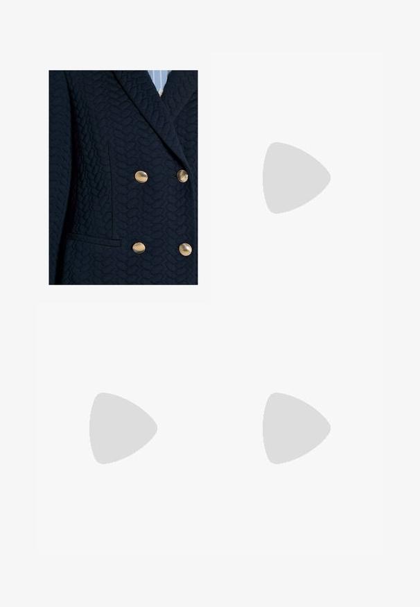 Blazer bleu marine foncé texturé avec quatre boutons dorés et un col à revers cranté porté sur une chemise rayée bleu clair.; Pull crème en maille torsadée avec une chemise à col blanc en dessous. Comprend des manches longues, des poignets et un ourlet côtelés. Motif tricoté texturé.; Jupe à carreaux en noir, blanc et gris avec des plis et une ceinture ajustée. Texture unie avec un motif tartan classique sur toute la surface.; Mocassin en cuir brun avec une semelle plate, orné d'un nœud et d'une breloque à franges à l'avant, présentant une texture lisse et un design épuré.