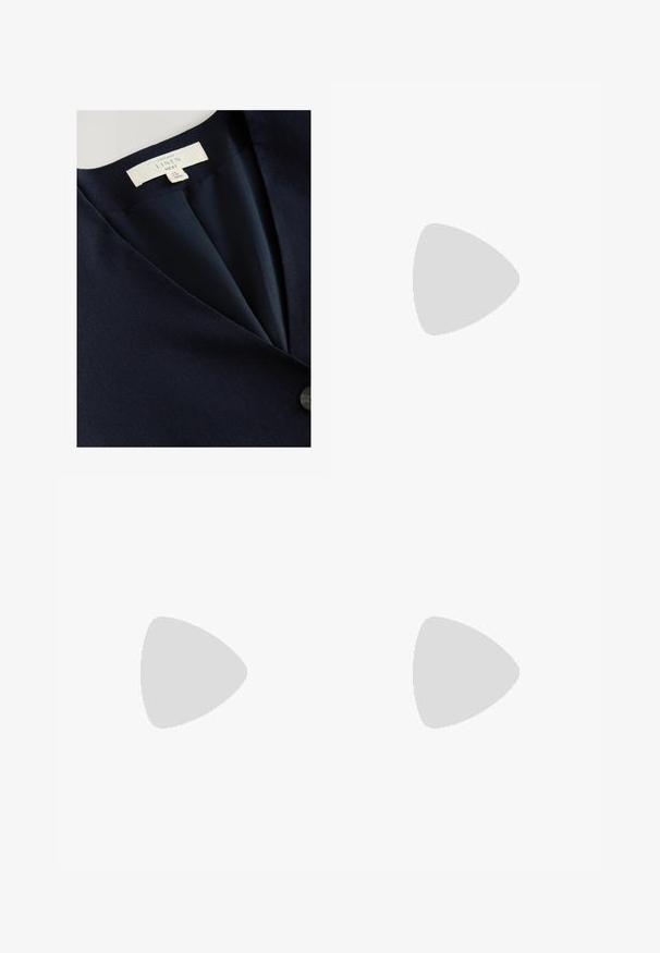 Blazer de lino navy con diseño de cuello en V, textura suave y cierre de un botón. Etiqueta de cuidado visible en el interior.; Camisa negra de manga larga con botones, cuello clásico, corte holgado y diseño liso, mostrada extendida sobre fondo blanco.; Pantalones de lino blancos con un ajuste relajado, que cuentan con una cintura elástica y cordones, y piernas rectas. Textura suave, tejido ligero.; Sandalia plana beige con tiras finas, decoración de cadena dorada en la tira delantera y pequeño colgante dorado en la hebilla del tobillo.