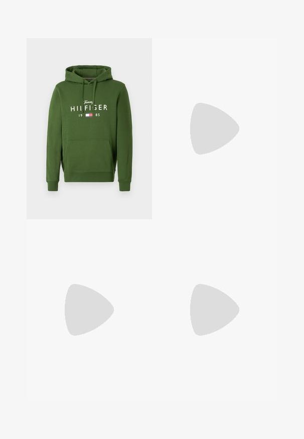 Grüne Kapuzenjacke mit Kängurutasche, verstellbarem Kordelzug-Hood und weißem Aufdruck mit dem Text "Tommy HILFIGER 1985" und einem Flaggenlogo.; Dunkelblaue Jeans aus Denim mit geradem Schnitt, ausgestattet mit einem standardmäßigen Bund, Fronttaschen und dezenten Stickdetails.; Weiße Leder-Sneaker mit perforierten Akzenten, flachen Schnürsenkeln und einem kleinen grünen Logo an der Seite. Gummisohle und gepolsterter Kragen für Komfort.; Person, die ein schwarzes Hemd trägt, hält mit der rechten Hand ihr linkes Handgelenk und zeigt ein silbernes Kreuz-Armband sowie einen silbernen Ring mit schwarzem Gesicht.