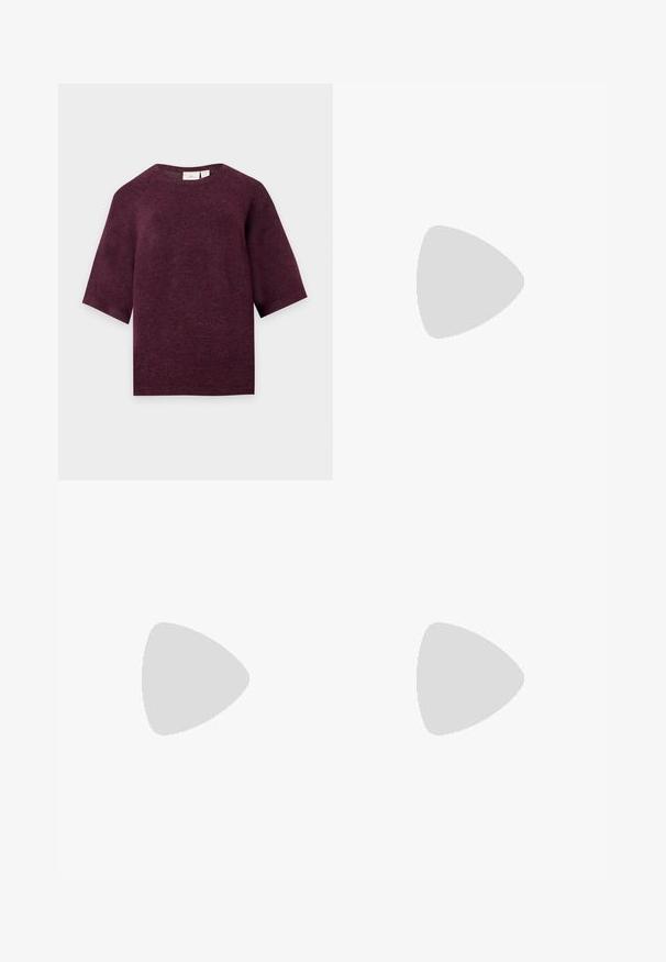 Dunkellila kurzärmeliger Strickpullover mit rundem Ausschnitt und geradem Saum, dargestellt auf hellem Hintergrund.; Schwarze Schlagjeans aus Denim mit Knopfverschluss, fünf Taschen und einer glatten Textur. Klassisches Design mit ausgestellt geschnittenem Saum.; Schwarze Wildleder- und Leder-Sneaker mit einem cremefarbenen Seiten-Swoosh und einer hellcremefarbenen Ferse. Ausgestattet mit beige Schnürsenkeln und einer Gummilaufsohle.; Frau trägt eine schwarz-weiß gemusterte Bluse und hält eine glänzende rote Schultertasche vor einem einfarbigen Hintergrund.