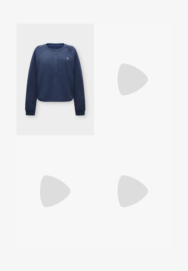Marineblå langærmet trøje med knappet henley-halsudskæring og lille hvid elg-logo på venstre bryst.; Vidbenede jeans i offwhite denim med høj talje, kobbernitter og klassisk design med fem lommer. Struktureret stof med rene kanter.; Hvid Adidas Samba sneaker med brune ruskindstriber, brun gummisål og beige ruskindståhætte, vist fra ydersiden på en ensfarvet baggrund.; Kvinde iført en sort- og hvidmønstret bluse, der holder en blank rød skuldertaske mod en ensfarvet baggrund.