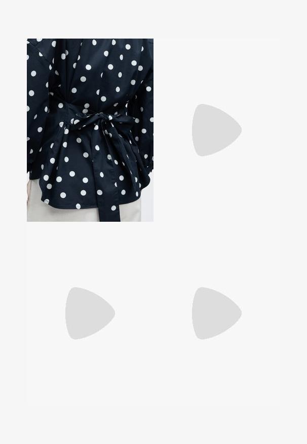 Gros plan d'un vêtement noir à pois blancs noué à la taille avec un nœud, montrant une partie des manches et de l'ourlet inférieur.; Pantalon à jambes larges avec fines rayures verticales noires et blanches, taille élastique et poches latérales sur un fond gris clair.; Chaussure Mary Jane en cuir verni noir avec un bout arrondi, une sangle au niveau de la cheville, un détail de boucle dorée et un petit talon carré. Texture lisse.; Sac à main beige structuré avec poignée supérieure, bandoulière détachable et boucle arquée couleur or sur un fond clair.