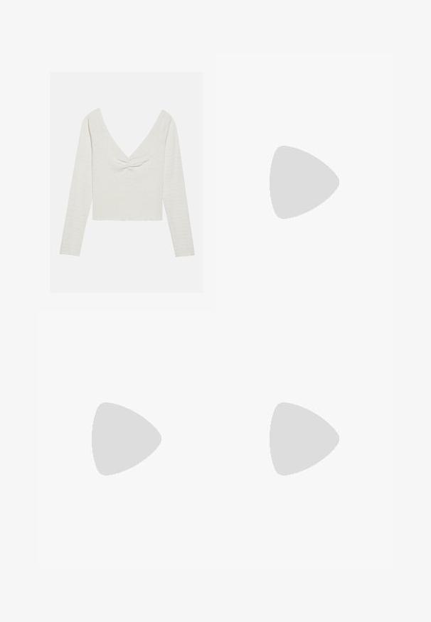 Langarm, off-white bovenstuk met een diepe V-hals en een geknoopte detail aan de voorkant, met een текстuurlijke stof en een cropped zoom.; Grijze denim flared jeans met een vervaagde afwerking, voorzien van een knoopsluiting, vijf zakken en gestikte details langs de tailleband en zoom.; Witte sportschoenen met roze accenten, gemaakt van suede en leer, met een ronde neus en een rubberen zool, weergegeven met lichtgekleurde sokken op een gele achtergrond.; Zilveren ketting met een ronde hanger waarin een centrale steen is verwerkt, versierd met een ronde rand. Inclusief een klein logo-tag aan de sluiting.