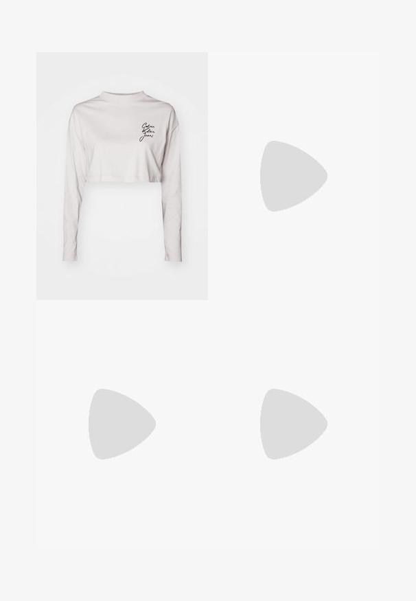 Geknipte lange mouwen shirt in lichtgrijze katoen, met een hoge hals en zwart "Calvin Klein Jeans" logo op de linkerkant van de borst.; Skinny jeans in mediumblauwe denim, met een hoge taille, zachte textuur, twee voorzakken en één achterzak.; Zwarte Calvin Klein hoge hak teenslipper die zweeft boven een betegeld buitenterrein met groen en een betonnen muur op de achtergrond.; Zwarte rechthoekige Calvin Klein handtas met enkele bovenriem, zilveren logo-ornament en een kleine klepsluiting aan de voorkant.