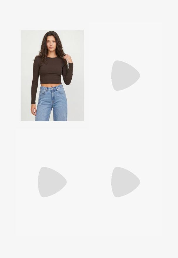 Jeune femme aux longs cheveux bouclés portant un crop top marron foncé à manches longues et un jean taille haute bleu clair sur un fond uni.; Jupe marron foncé, longueur cheville, forme trapèze avec une texture lisse et unie et une taille ajustée sur un fond blanc uni.; Chaussure plate en cuir bordeaux foncé avec un bout pointu et une fine bride en T avec une boucle argentée sur fond blanc.; Petit sac à main noir brillant avec deux longues anses et des détails à cordon sur les côtés sur un fond clair uni.