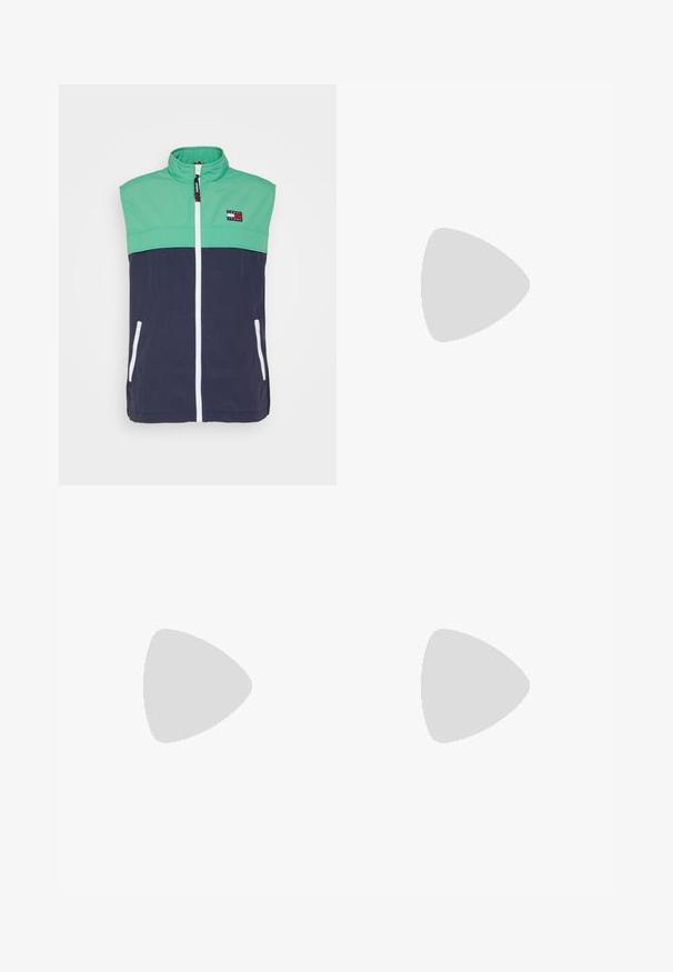 Veste sans manches avec une section supérieure verte et une section inférieure marine, dotée d'un col haut, d'une fermeture éclair blanche et de poches latérales. Patch logo distinctif.; T-shirt blanc manches courtes col rond avec logo GANT, écusson rayé rouge et blanc, "1949" et texte "American Sportswear" sur le devant.; Jean slim droit bleu avec cinq poches, fermeture par bouton et fermeture éclair, et décoloration subtile aux cuisses et aux genoux.; Baskets basses blanches en cuir lisse. Dotées d'un talon en bleu marine et d'un accent rouge sur la semelle. Six œillets pour les lacets.