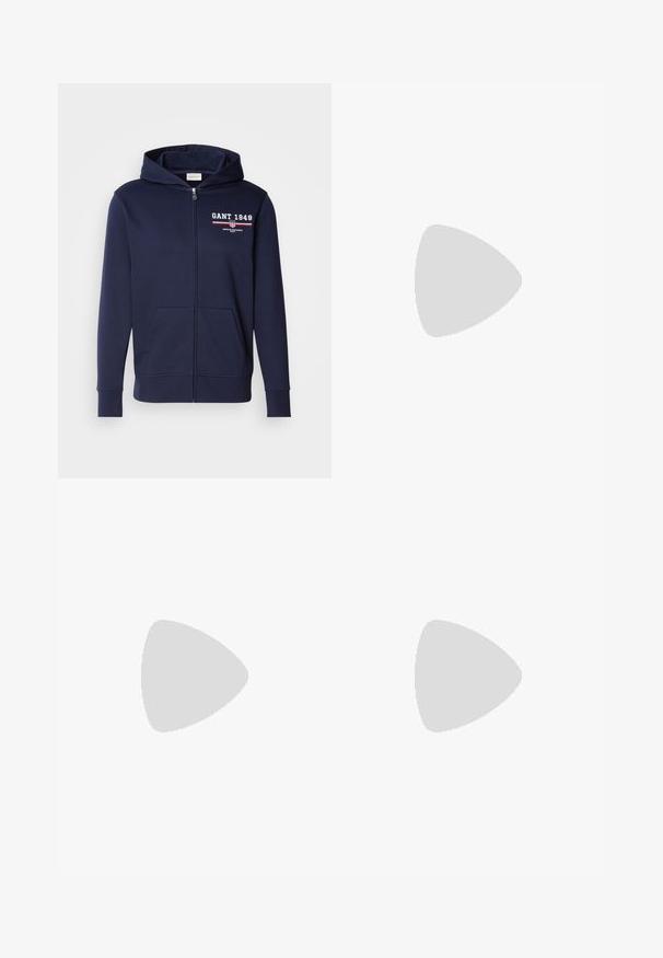 Sweat à zip bleu marine en tissu doux, avec le logo "GANT 1949" en blanc et rouge. Comprend des poches avant et une capuche avec cordon de serrage.; T-shirt en coton blanc avec un col rond, des manches courtes et un logo imprimé. Présente un design minimaliste et une coupe décontractée.; Pantalon en coton beige avec une coupe droite, présentant une fermeture à bouton et des plis sur le devant pour plus de détails.; Baskets blanches avec des accentuations en daim beige et des semelles en caoutchouc clair ; présente un design low-top et des détails texturés sur la tige.