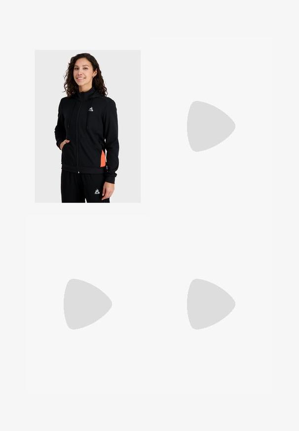 Felpa nera con zip, realizzata in tessuto morbido, dotata di un colletto alto, tasche frontali e dettagli laterali arancioni. Logo esposto sul petto.; Maglietta in cotone bianco con vestibilità rilassata, maniche corte e un piccolo logo ricamato sul lato sinistro del petto.; Pantaloni sportivi bianchi a gamba larga con vita a coste e delicato dettaglio del logo. Tessuto liscio con vestibilità rilassata e orlo affusolato.; Scarpe sportive nere con tomaia testurizzata, dettagli argentati e suola con motivo, abbinate a un lungo indumento nero. Ambientate su un tappeto blu.