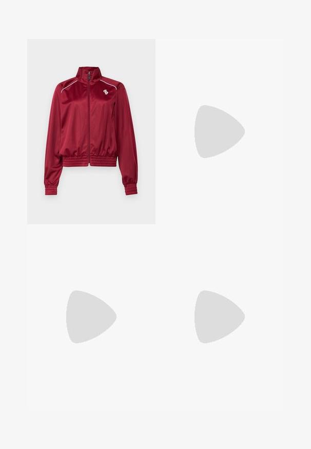 Red satin jacket with a high collar, front zipper, and ribbed cuffs. Features white accents and a small logo on the left chest.; Red cotton t-shirt with a round neckline, short sleeves, white three-stripe accents on shoulders, and a small white logo on the chest.; Orange athletic pants made of smooth fabric, featuring a wide-leg design, elastic waistband, and contrasting side stripes.; Red suede sneakers featuring pink accents, white three-stripe logo, and red laces. Worn with white ribbed crew socks on a green surface.