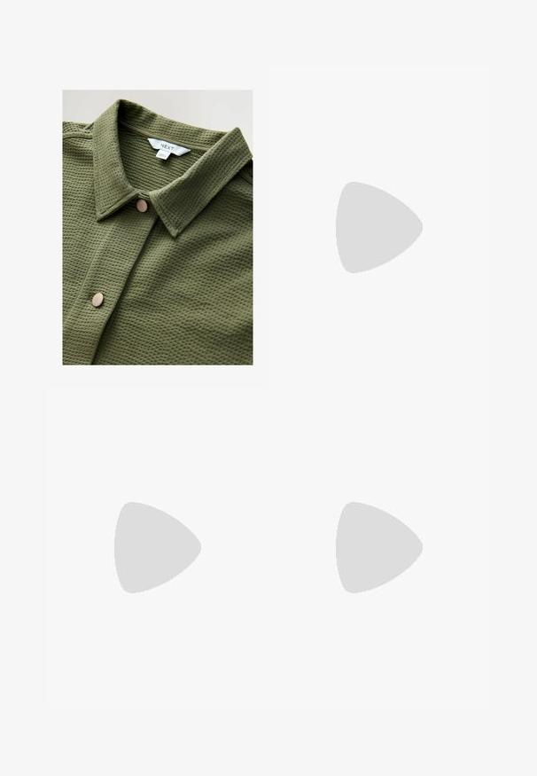 Maglietta in maglia a nido d'ape verde oliva con colletto a punta e un singolo bottone tondo beige sul davanti. Etichetta con la scritta "NEXT". Texture morbida.; Camicetta bianca con spalline sottili, design a V, texture liscia, silhouette aderente, abbinata a leggings verdi oliva a vita alta.; Pantaloni beige a gamba larga realizzati in un tessuto resistente, con ampi tasconi frontali, una cintura intrecciata e dettagli di cucitura sottili.; Scarpe slip-on con stampa leopardata e suola spessa marrone, abbinate a jeans a gamba larga blu, poggiate su un pavimento in legno.