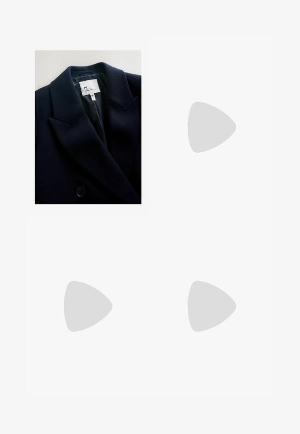 Dark navy blazer with a textured fabric, sharp lapels, and a dual-button closure. Interior features a smooth lining and brand label.; Navy sleeveless top with a ribbed texture, featuring a rounded neckline and four decorative buttons on the left shoulder.; Wide-leg pants in dark navy, featuring a textured fabric, drawstring waistband, and loose silhouette for comfort.; Red suede sneaker with white stripes, lace-up design, and textured brown rubber sole. Worn with black pants, set against blue carpet.; White fleece scarf with fringed edges, soft texture, and rectangular shape. Suitable for layering and providing warmth.