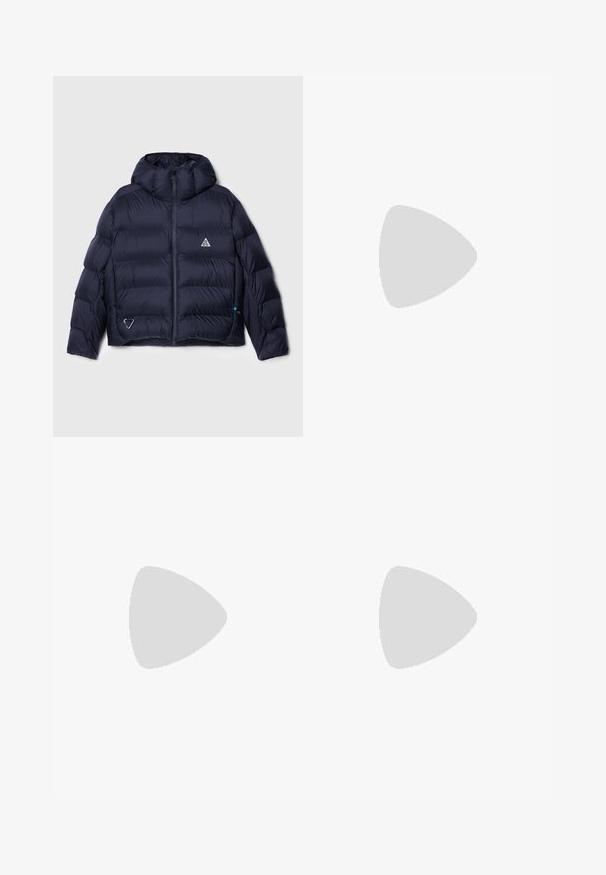 Marineblauwe pufferjack met een capuchon, voorzien van een doorgestikt ontwerp, ritssluiting en een logo op de borst. Inclusief een zijzak met hardware details.; Afgekorte ribgebreide top in donker marineblauw, met een hoge halslijn en een subtiele Nike-logo. De stof heeft een gestructureerde, rekbare uitstraling.; Beige linnen broek met een ontspannen pasvorm, voorzien van zijzakken en decoratieve stikseldetails, naadloze tailleband en rechte pijpen.; Bruine en crèmekleurige sneakers van suède en leer, met een geperforeerde neus, veters en witte zolen. Draagt met witte broek.
