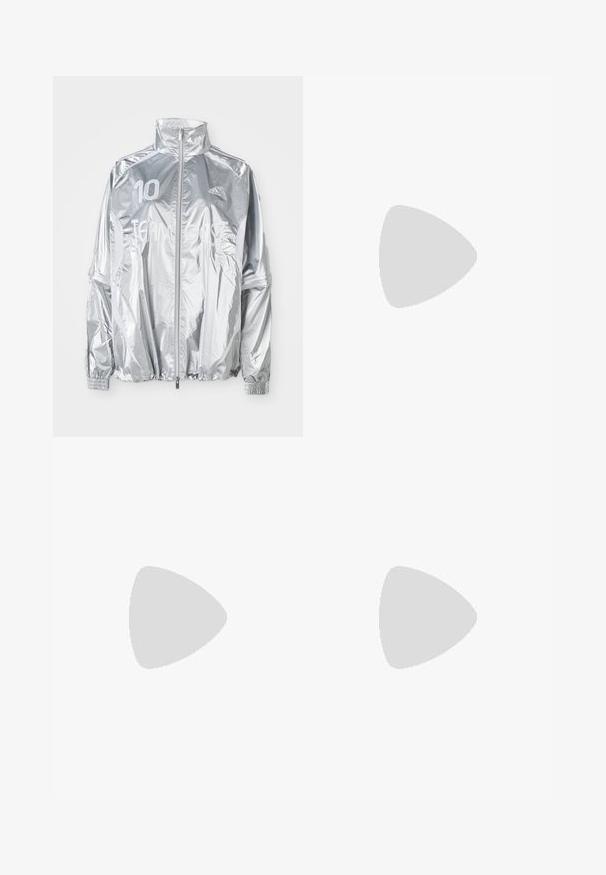 Strieborná Adidas bunda na zips s vysokým golierom, elastickými manžetami, číslom "10" na ľavom prse a textom "TEAM GAST" na prednej strane.; Biela bavlnená tričko s krátkymi rukávmi a okrúhlym výstrihom. Obsahuje čierne logo Adidas na hrudi a kontrastný čierny vnútorný golier.; Krémové mikinové nohavice s voľným strihom, so tmavohnedými bočnými pruhmi a vyšitým logom na ľavom stehne.; Tenisky Adidas Gazelle so smotanovým semišovým horným dielom, modrými koženými akcentmi, tromi modrými pruhmi, béžovou medzipodrážkou a hnedou gumovou podrážkou.