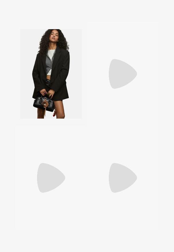 Jeune femme aux cheveux bouclés portant un blazer noir superposé et un top court, tenant un sac à main noir orné de porte-clés.; Haut court à manches courtes de couleur marron avec un ourlet légèrement arrondi. Texture douce et coupe décontractée, présentant un col rond et des coutures minimales.; Pantalons larges marron en tissu doux, avec une taille élastique et un cordon de serrage, et deux poches latérales.; Baskets en daim marron avec des bandes en cuir blanc, semelle en caoutchouc, bout arrondi et lacets. Comprend un logo sur la languette et des accents perforés.