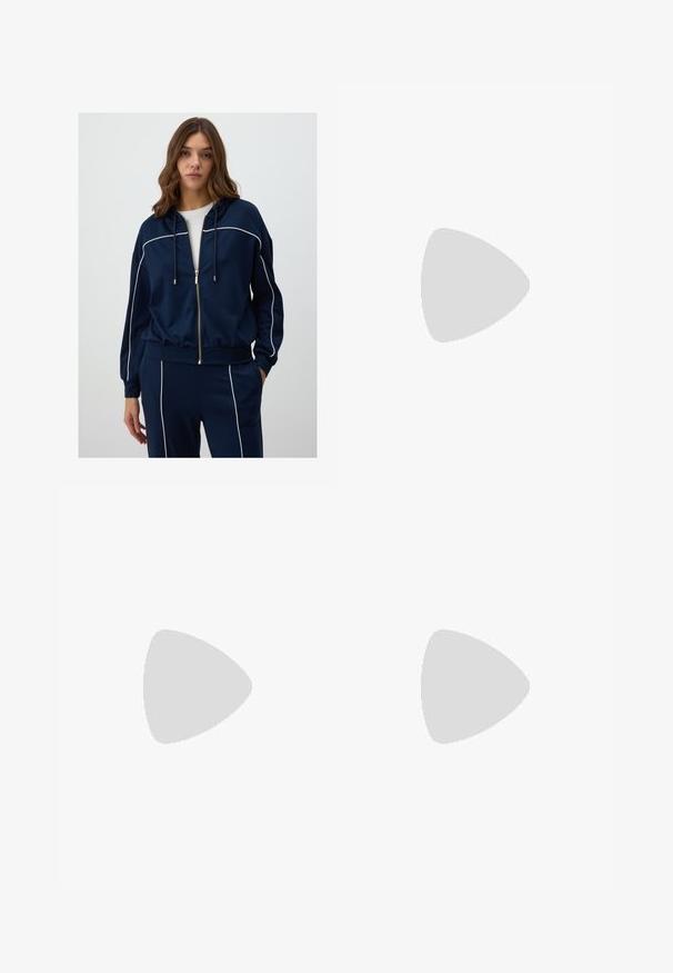 Felpa con zip di colore blu navy, realizzata in tessuto morbido, con piping bianco lungo le spalle e le maniche, dotata di cappuccio regolabile e vestibilità comoda.; T-shirt in cotone nero con vestibilità rilassata, maniche corte, scollatura arrotondata e una texture liscia. Nessuna trama o accento visibile.; Pantaloni neri a gamba dritta, con tasche frontali e spacchi laterali all'orlo. Realizzati in tessuto morbido e liscio. Adatti a diverse occasioni.; Sandali con tacco in vernice nera, con punta squadrata, cinturini alla caviglia e fibbie in argento. Presentano un tacco a blocco spesso per maggiore stabilità.