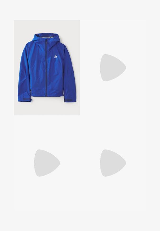 Modra vodoodporna jakna s kapuco, zadrgo, nastavljivimi manšetami in detajlom logotipa v obliki trikotnika. Ima gladko, lahko tkanino.; Črna bombažna majica s kratkimi rokavi, ki na sprednji strani nosi bel print številke "95" in kontrastno šivanje ob robovih.; Črne široke hlače s elastiko v pasu in malim belim logotipom Nike. Tkanina ima gladko teksturo, zasnovano za udobje in sproščeno nošenje.; Črne športne čevlje z teksturirano zgornjimi deli, srebrnimi odtenki in z vzorčenim podplatom, v kombinaciji z dolgim črnim oblačilom. Postavljeno na modrem preprogo.