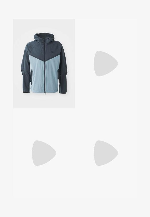 Bunda s kapucí, předním zipem, designem v tmavě modré a světle modré barvě s bloky a bočními kapsami na zip.; Bílý bavlněný tričko s krátkým rukávem a kulatým výstřihem. Na levé horní části hrudi je vytištěno černé logo "Carhartt".; Černé lehké cargo kalhoty s elastickým pasem, bočními zipy a prostornými kapsami. Mají volný střih a zúžené manžety.; Bílé sportovní boty s texturovanými překryvy, masivní podrážkou a šedými akcenty. Na nohou mají bílé ponožky a zelené šortky na modrém povrchu.